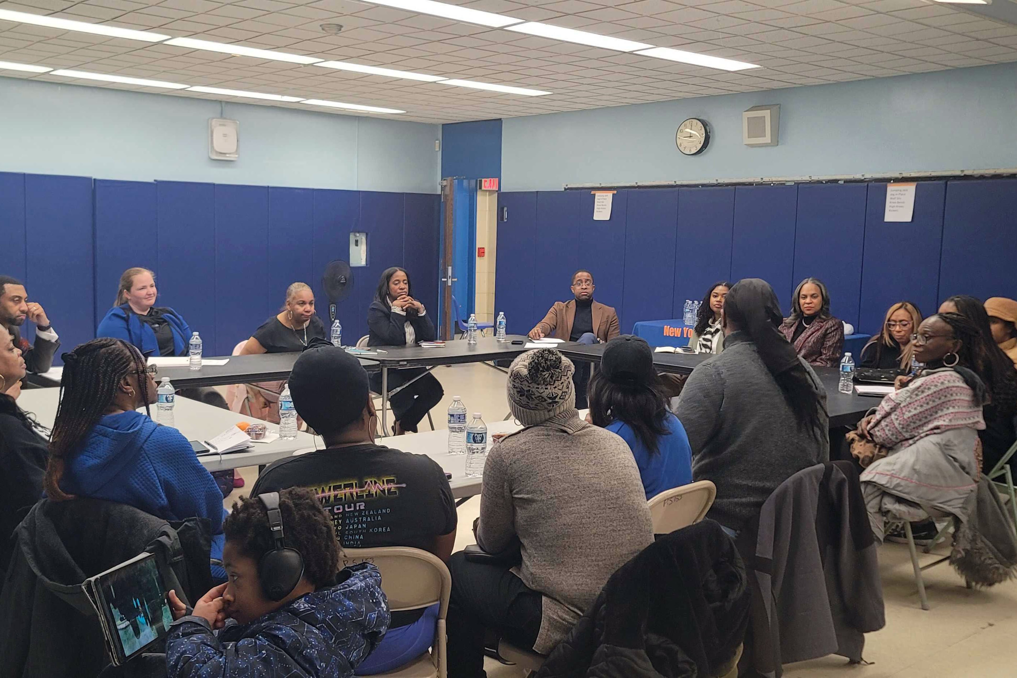 A large group of adults sit around tables in a blue room.