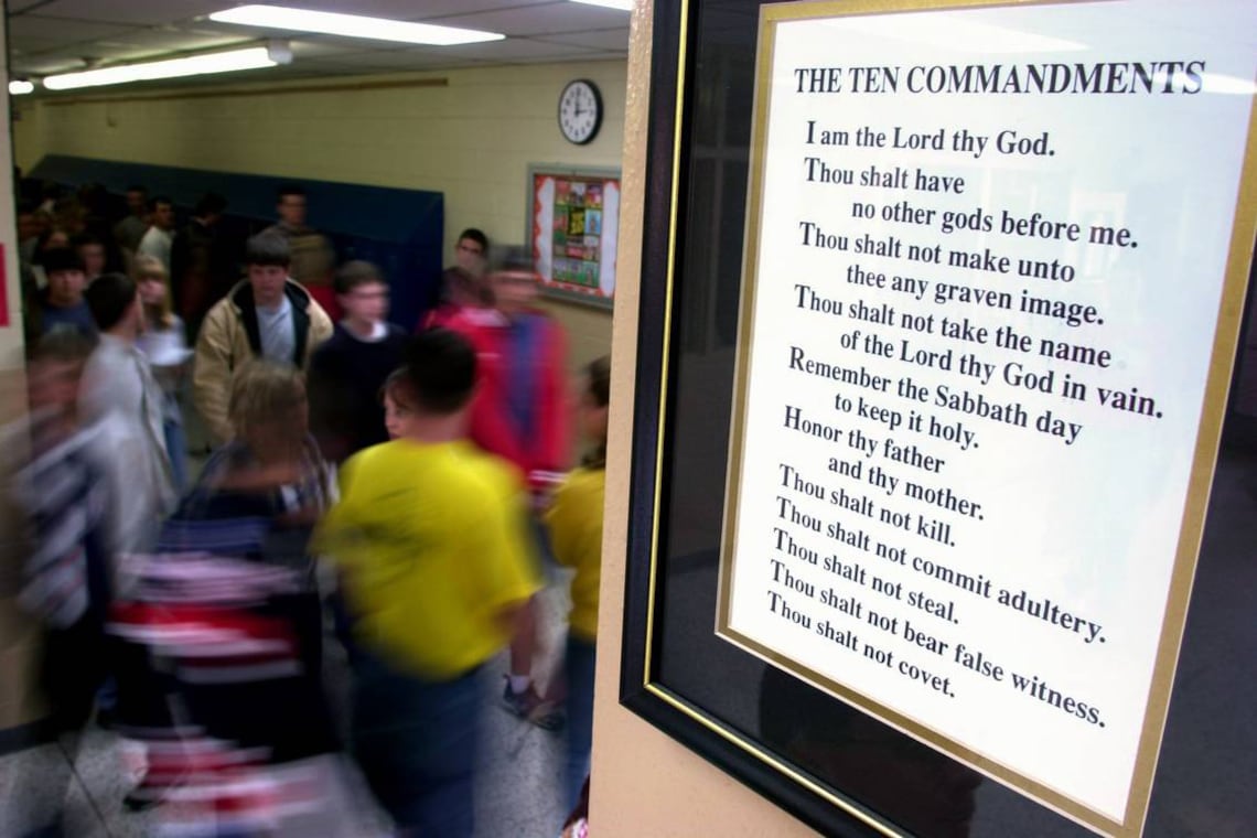 A photograph of a busy high school hallway with a large poster of the Ten Commandments on the wall.