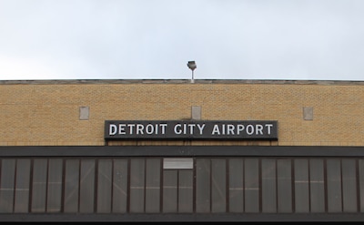The top of the outside of a tan brick and glass building with a sign at the top that reads "Detroit City Airport."