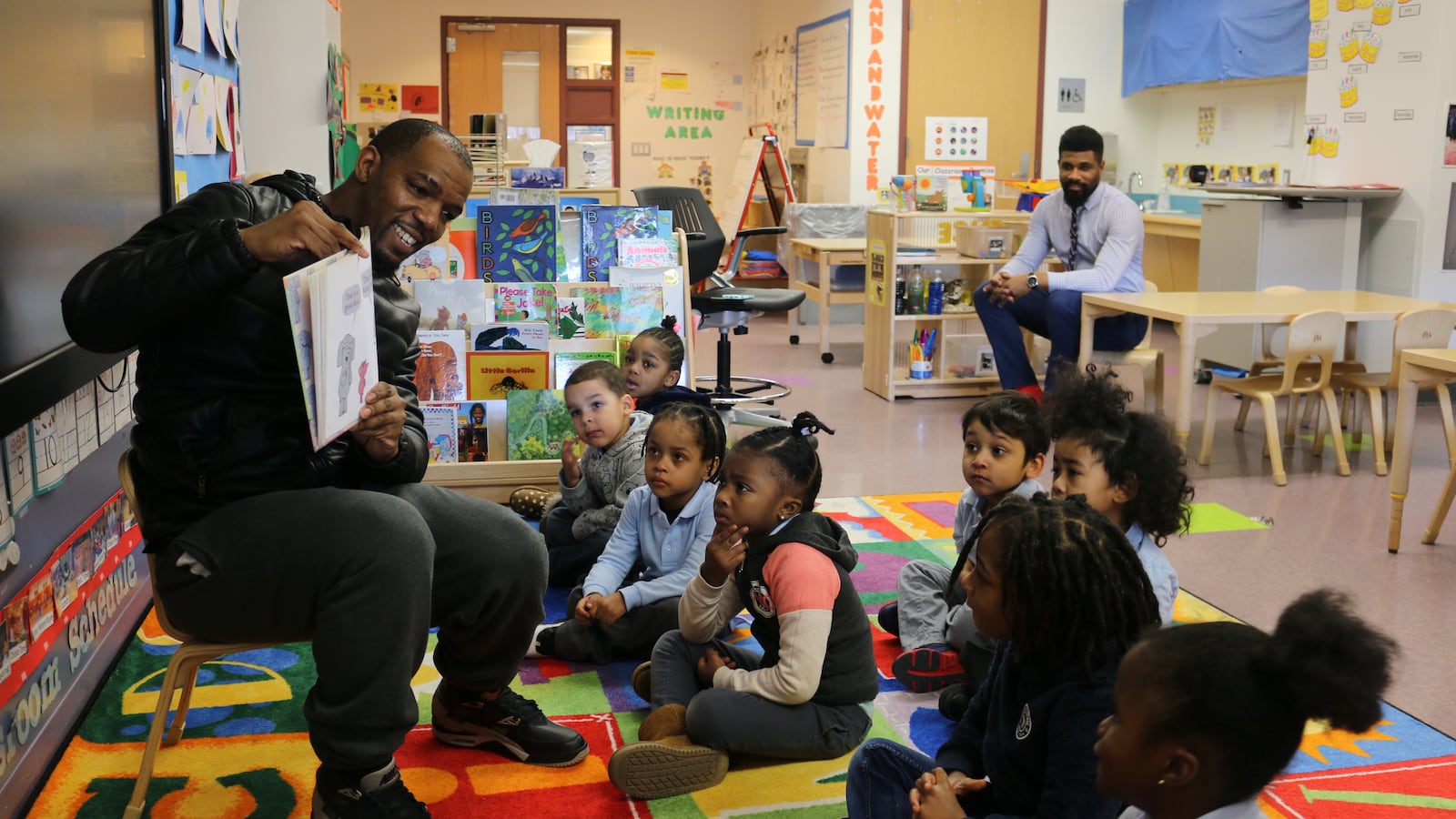Alphonzo Macon reads to his son's pre-K class at Learning Through Play in the South Bronx. Assistant Principal Anthony Tucker, back right, invites father figures to take an active role in the school to help build students' literacy skills.