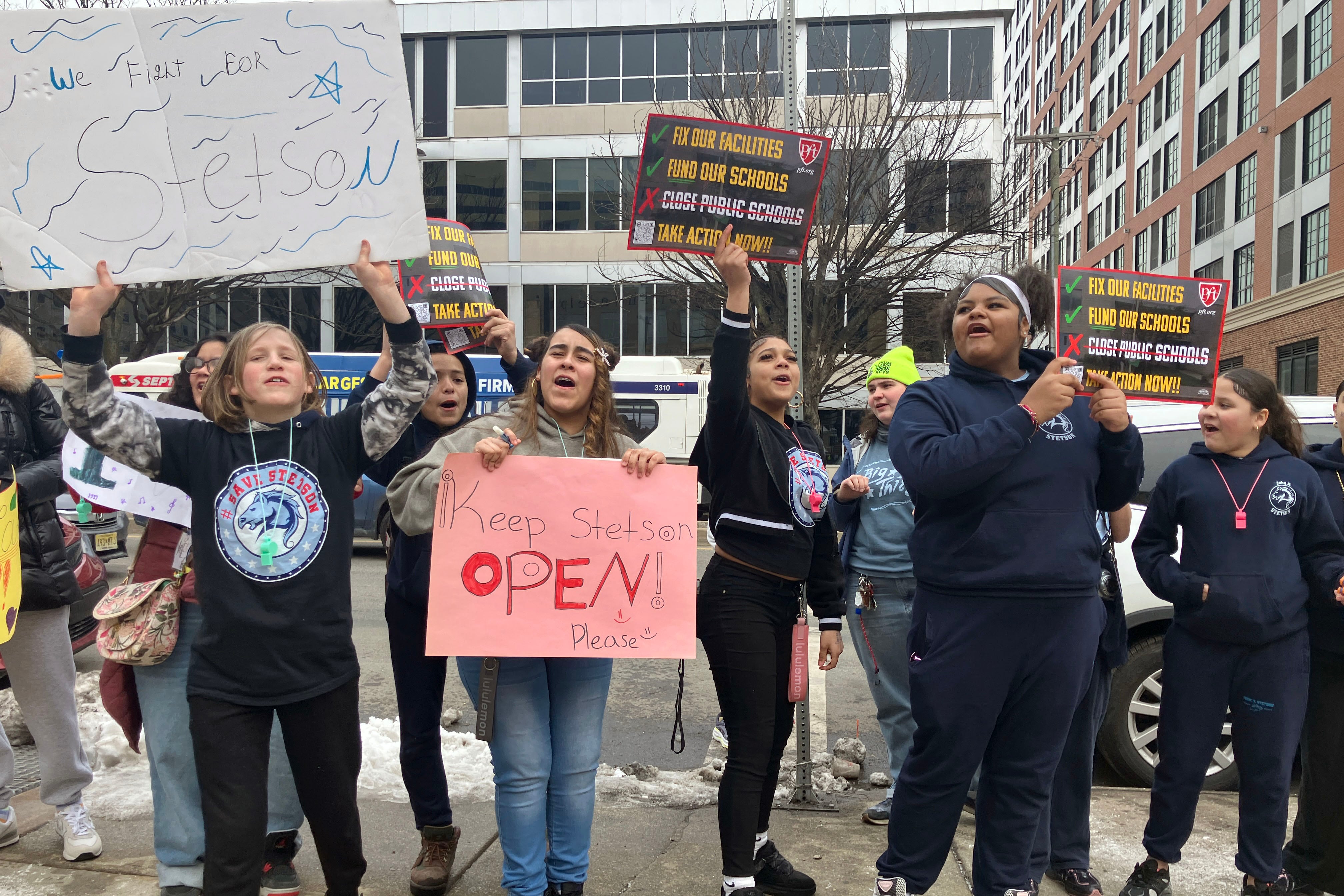 A photograph of a large group of students holding protest signs standing outside.