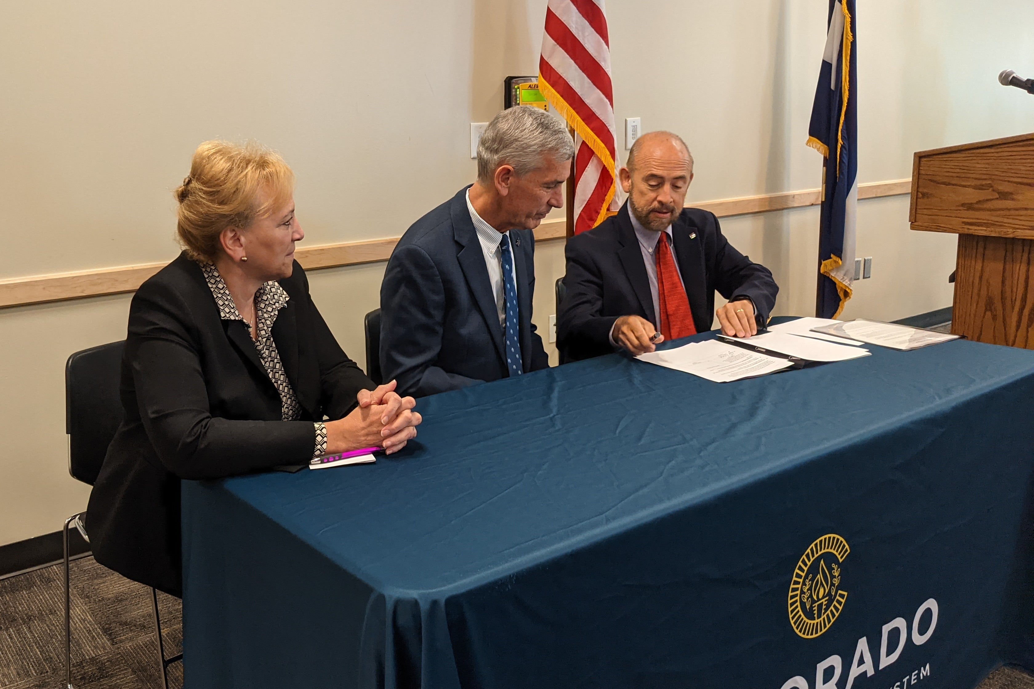 Three Colorado college leaders dressed in suits sit at a table with blue cloth to sign a document that formalizes a partnership between community colleges and the Colorado School of Mines.