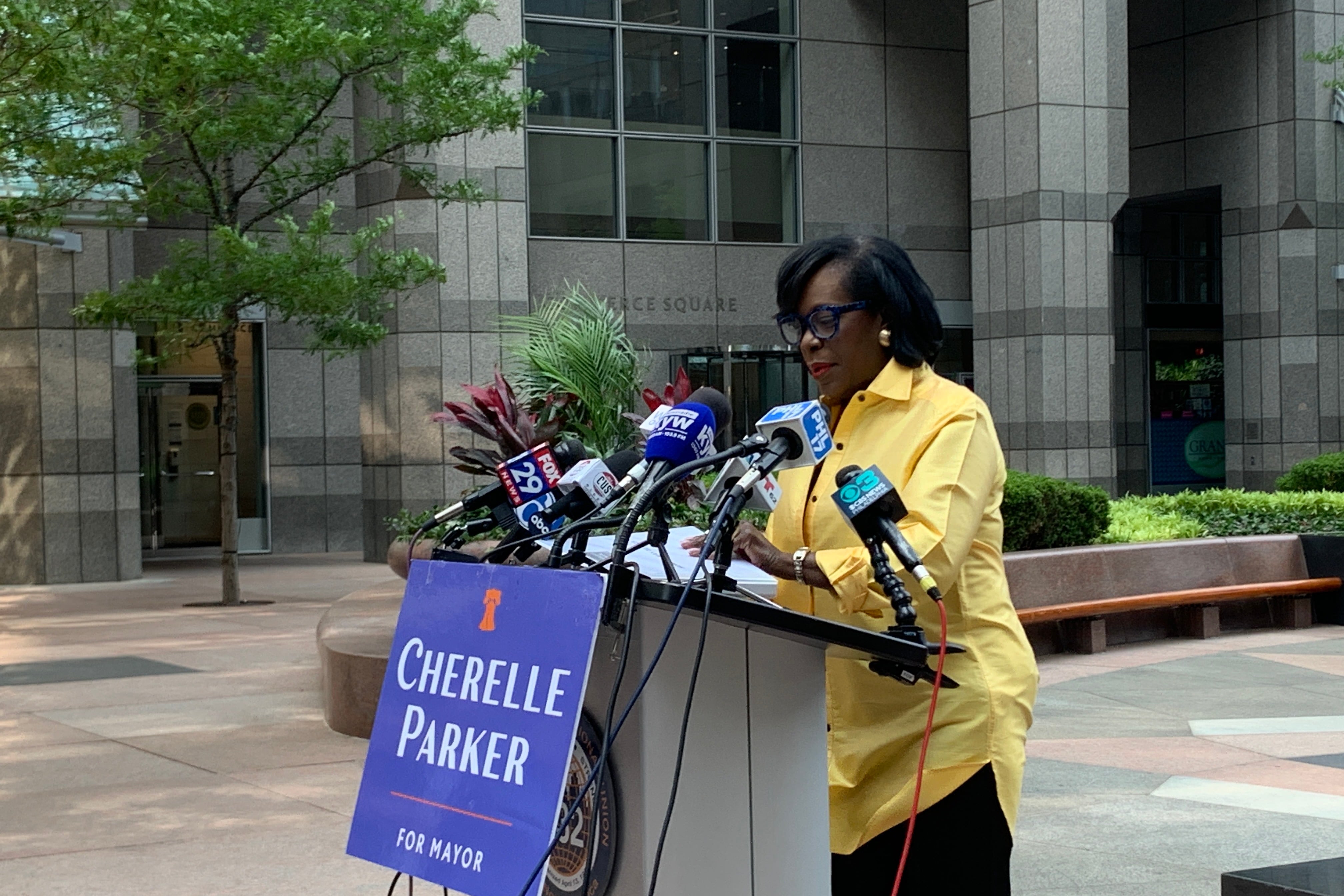 A woman in a yellow shirt and black pants speaks at a podium.