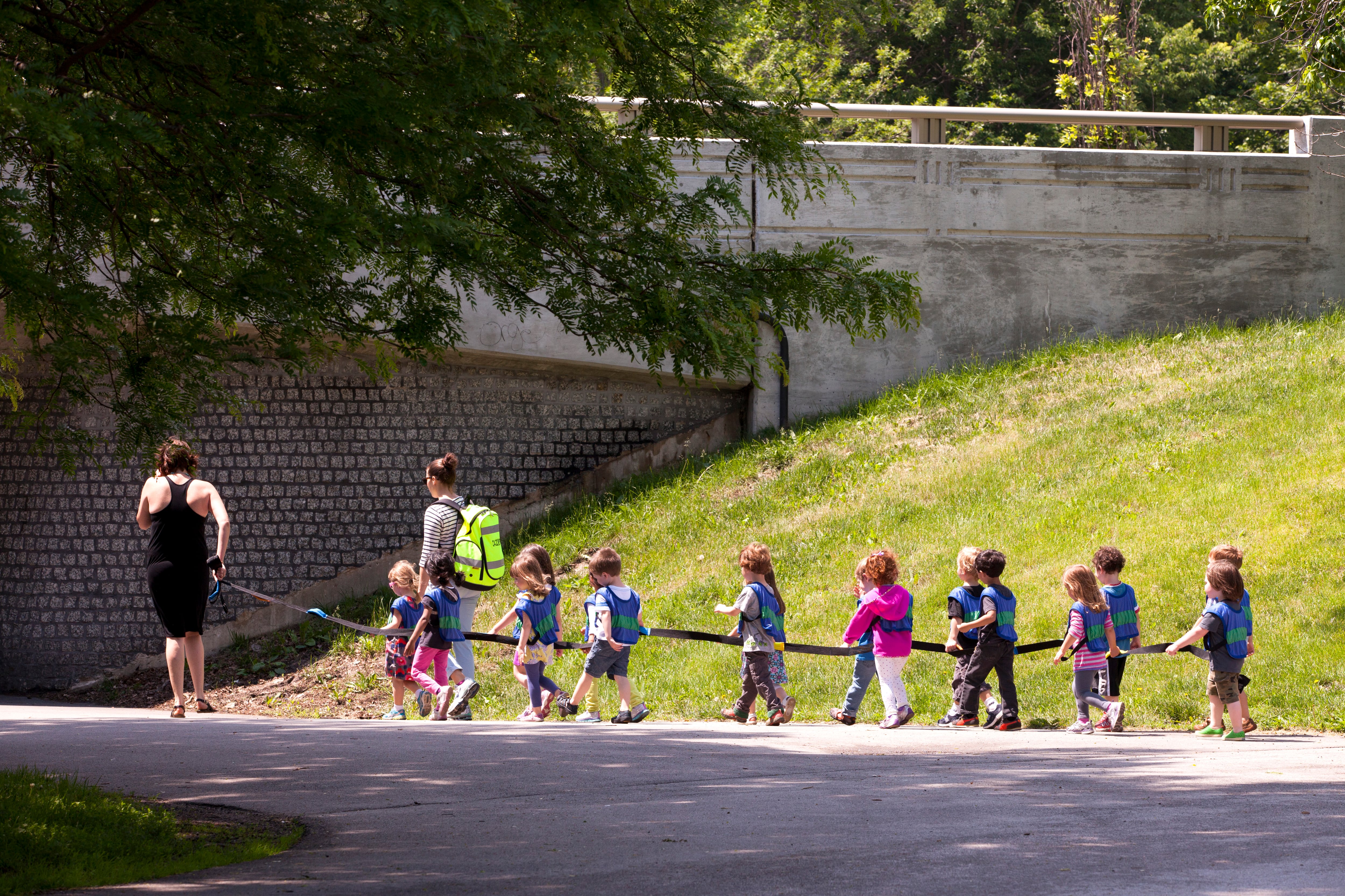 Daycare children on a long leash and their caretakers enjoy a walk through a Chicago park