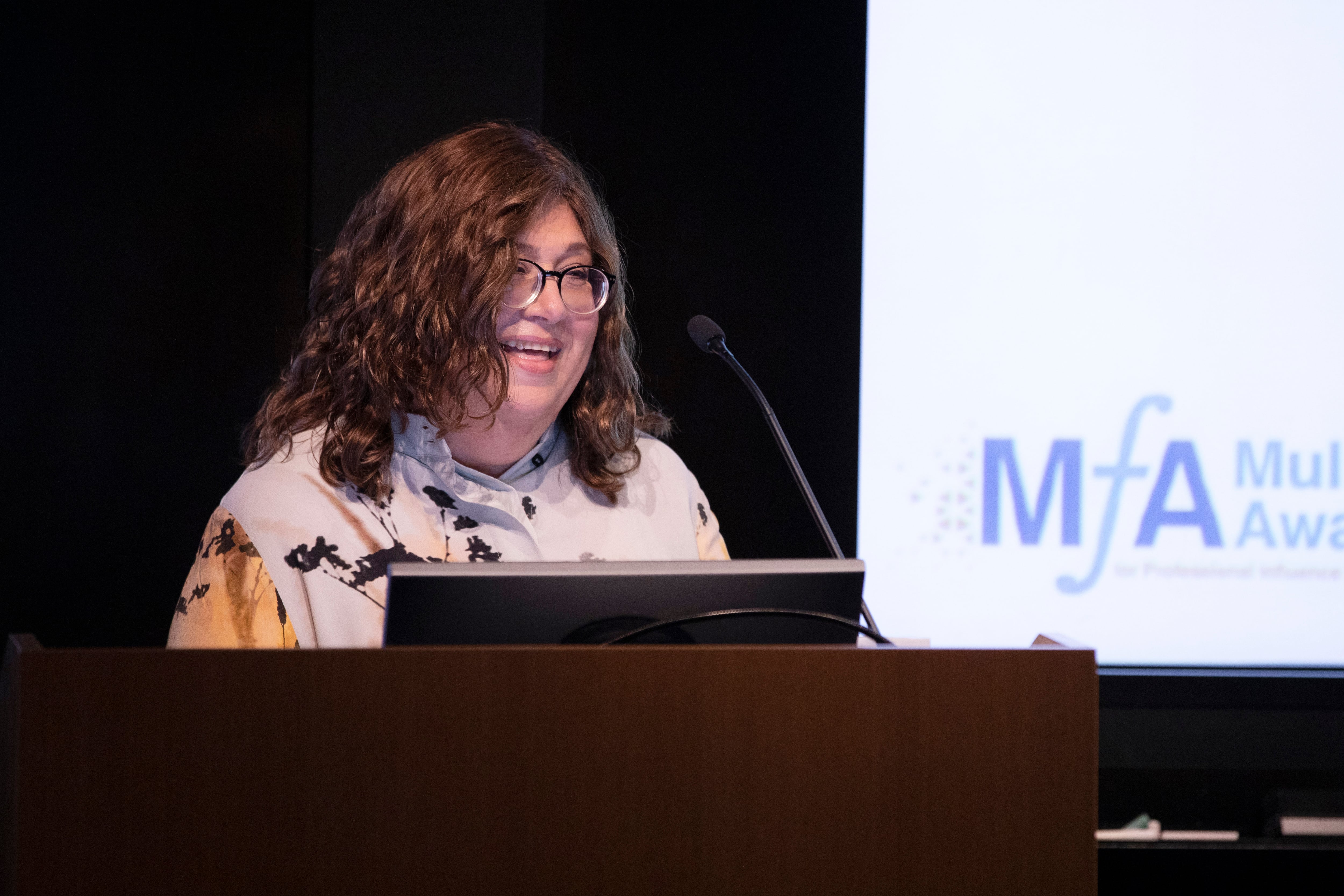 A woman in glasses stands at a podium.