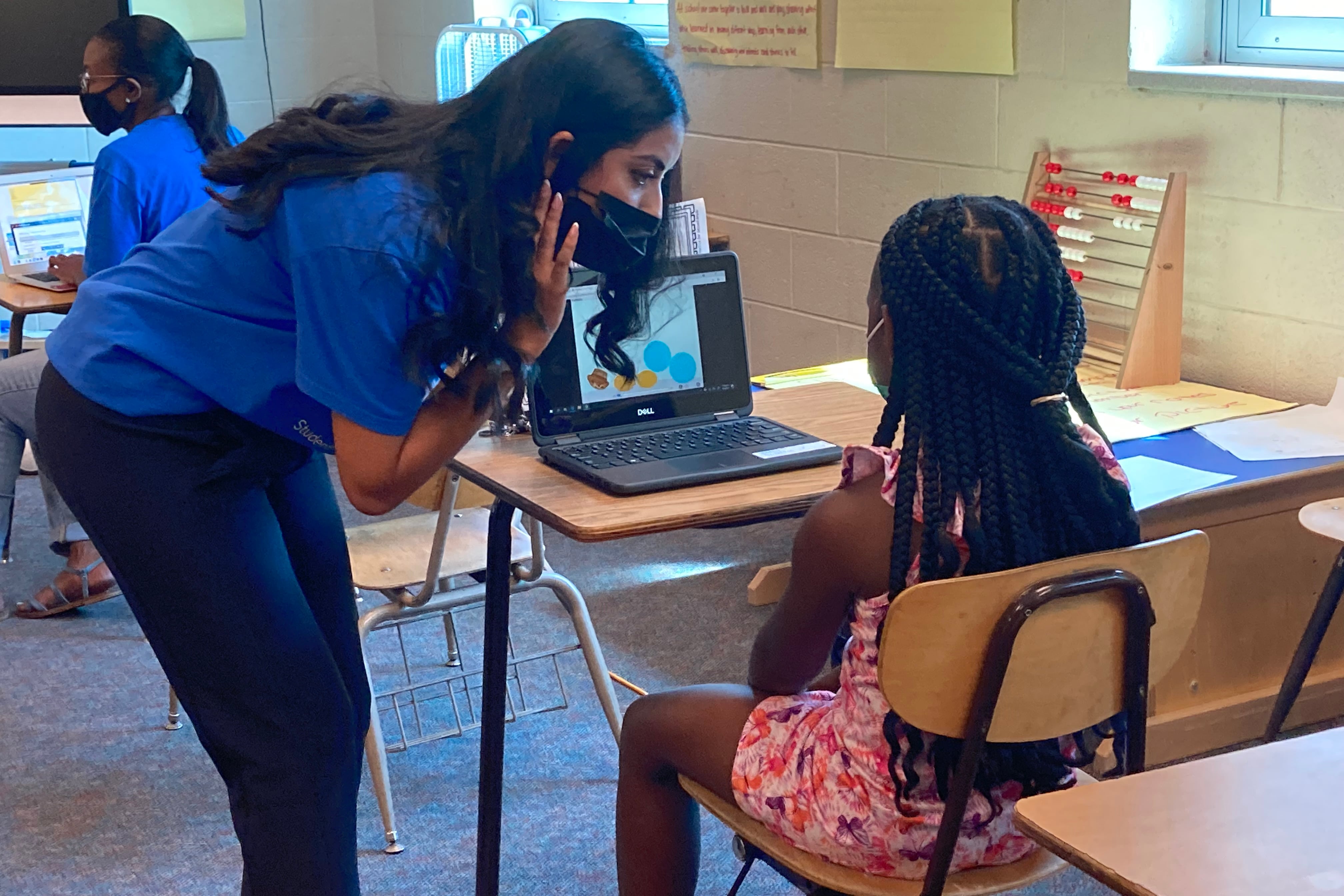 A teacher leans over to help a student with a summer school exercise at Brenda Scott Academy in the Detroit school district.