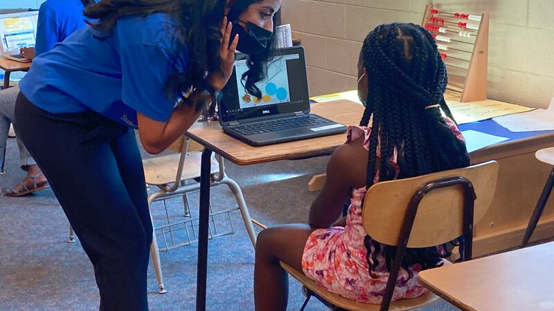 A teacher leans over to help a student with a summer school exercise at Brenda Scott Academy in the Detroit school district.