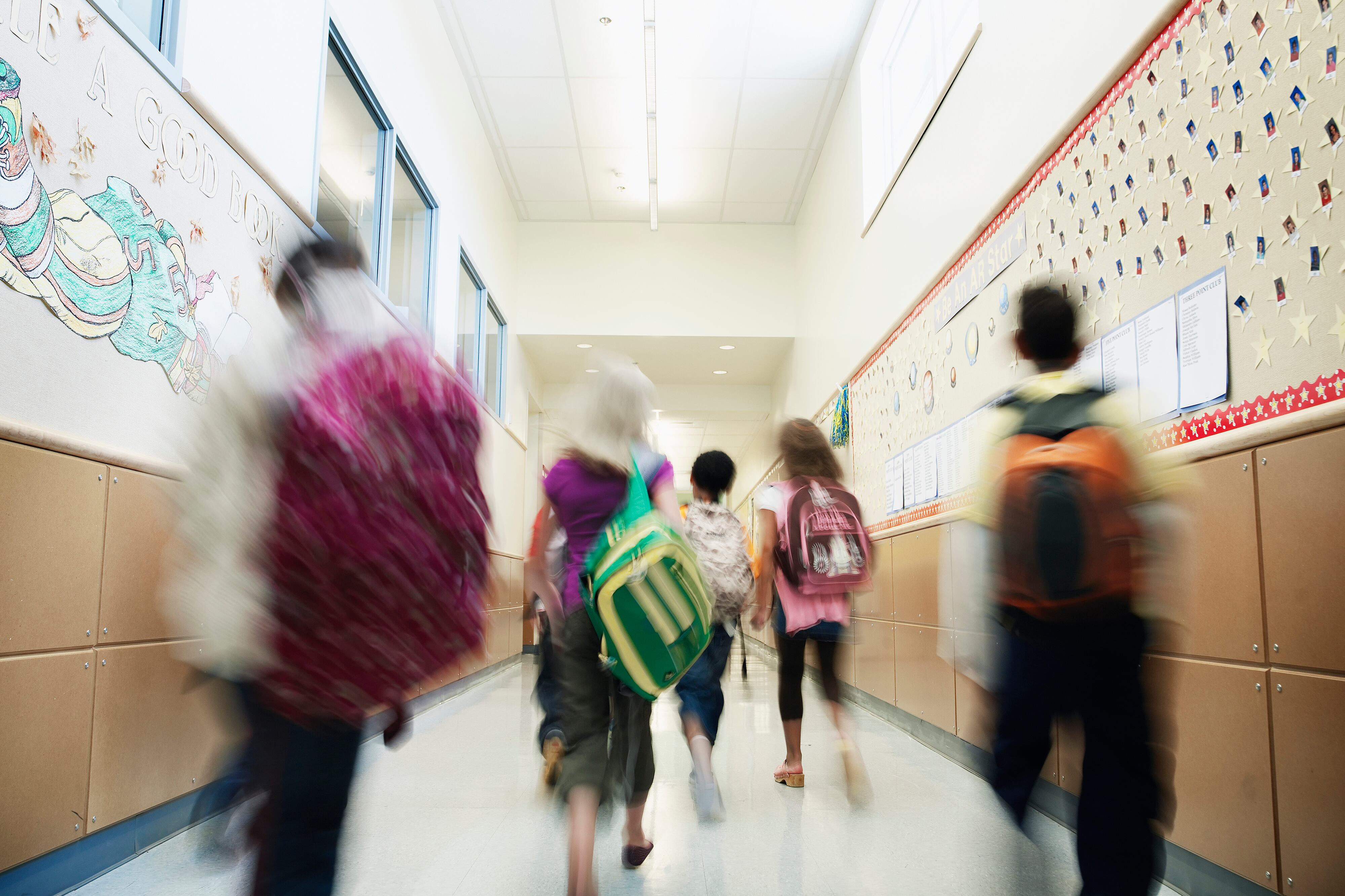 A group of middle school students walk away from the camera in a blurry motion down a school hallway.