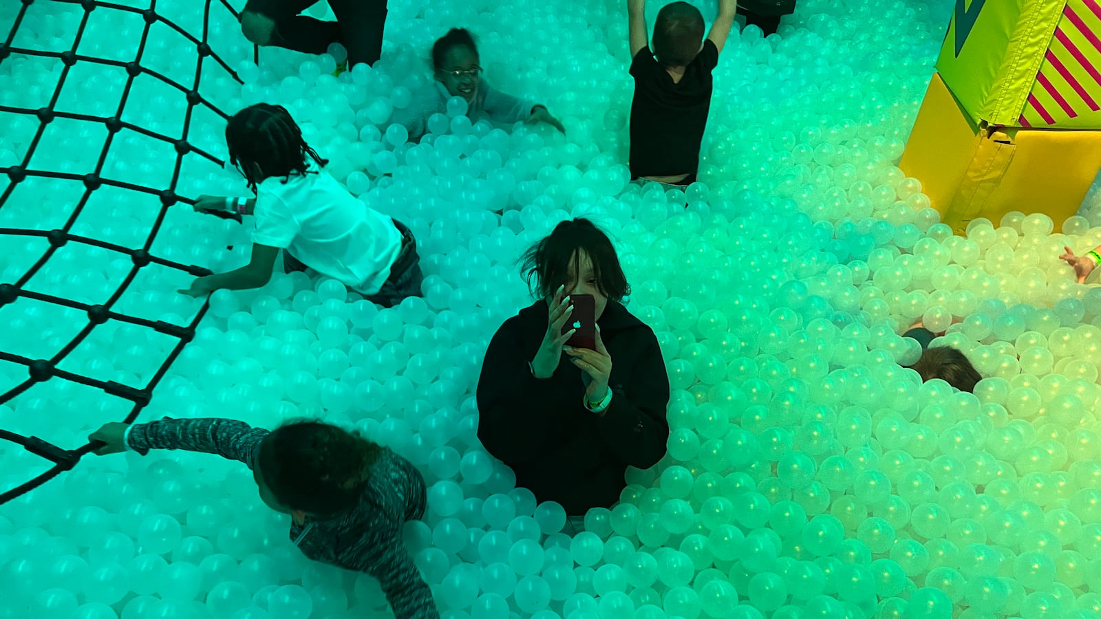 Several children and one teenager are in a ballpit.