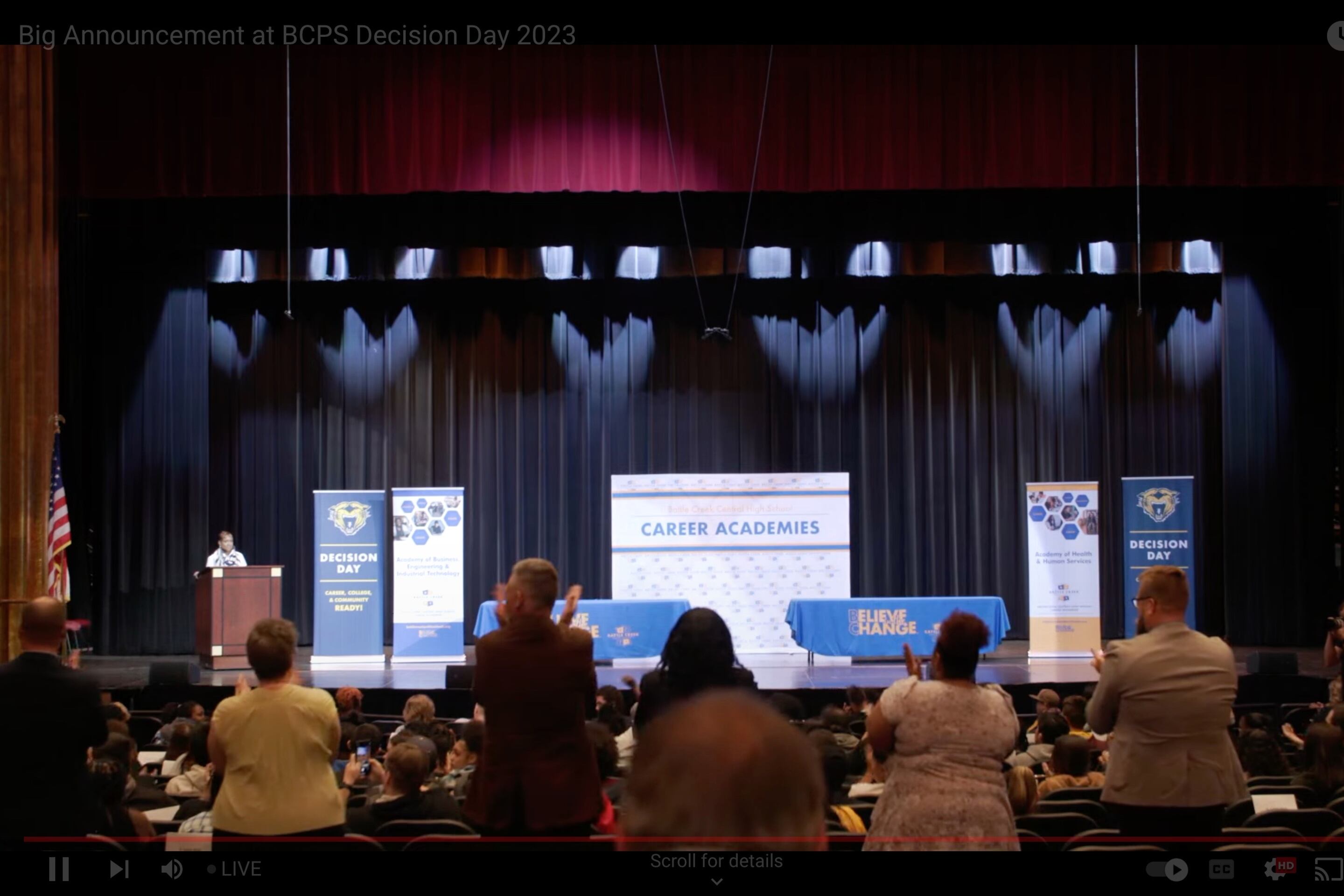 People clapping and standing after the announcement of a new scholarship program.