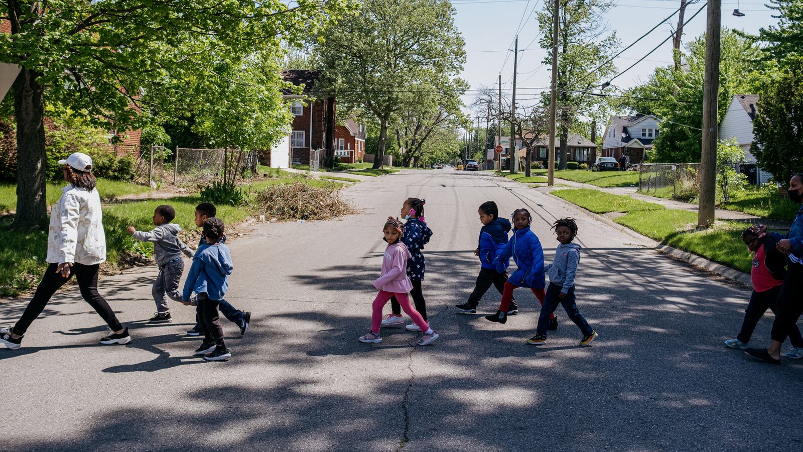 A teacher leads a group of preschool students across a street during a walk around the neighborhood.