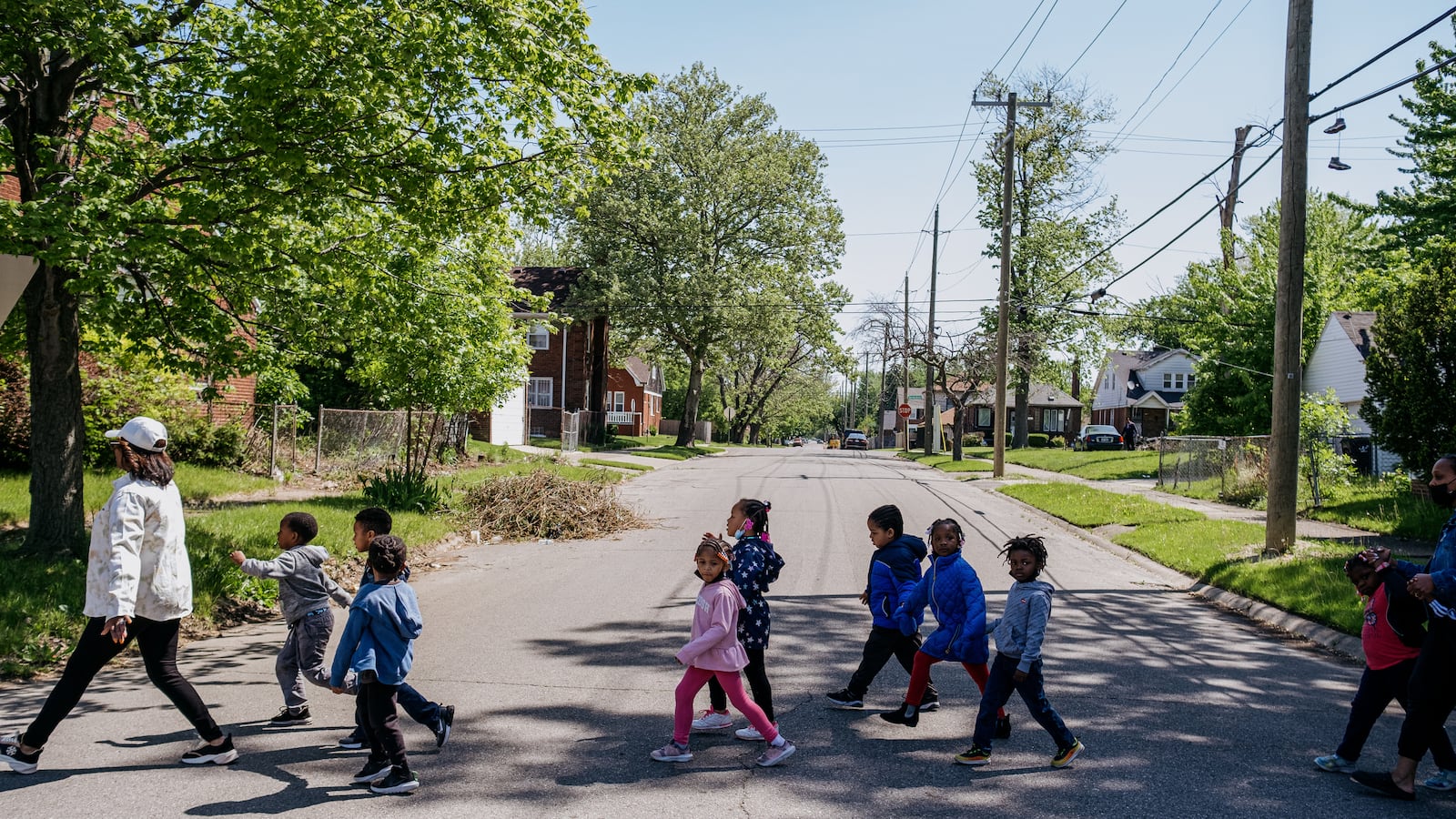 A teacher leads a group of preschool students across a street during a walk around the neighborhood. 