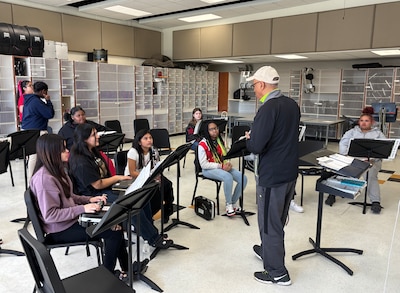A man stands in front of a middle school music classroom full of students.