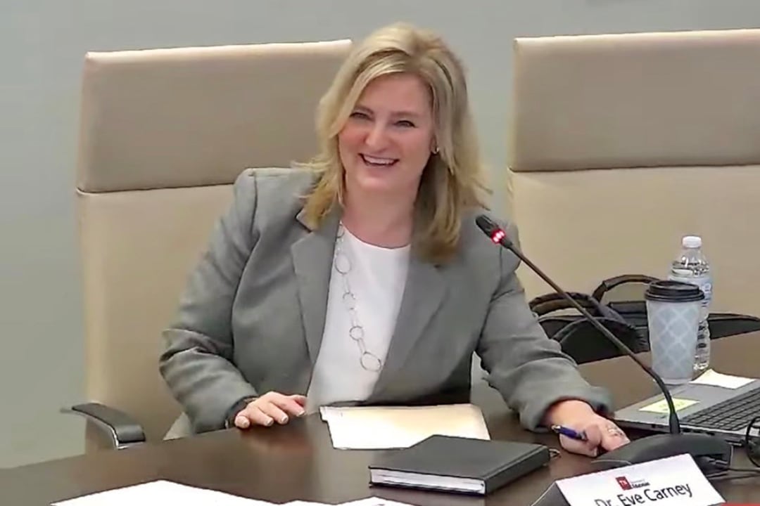 woman in gray suit and white shirt sits in tan chair