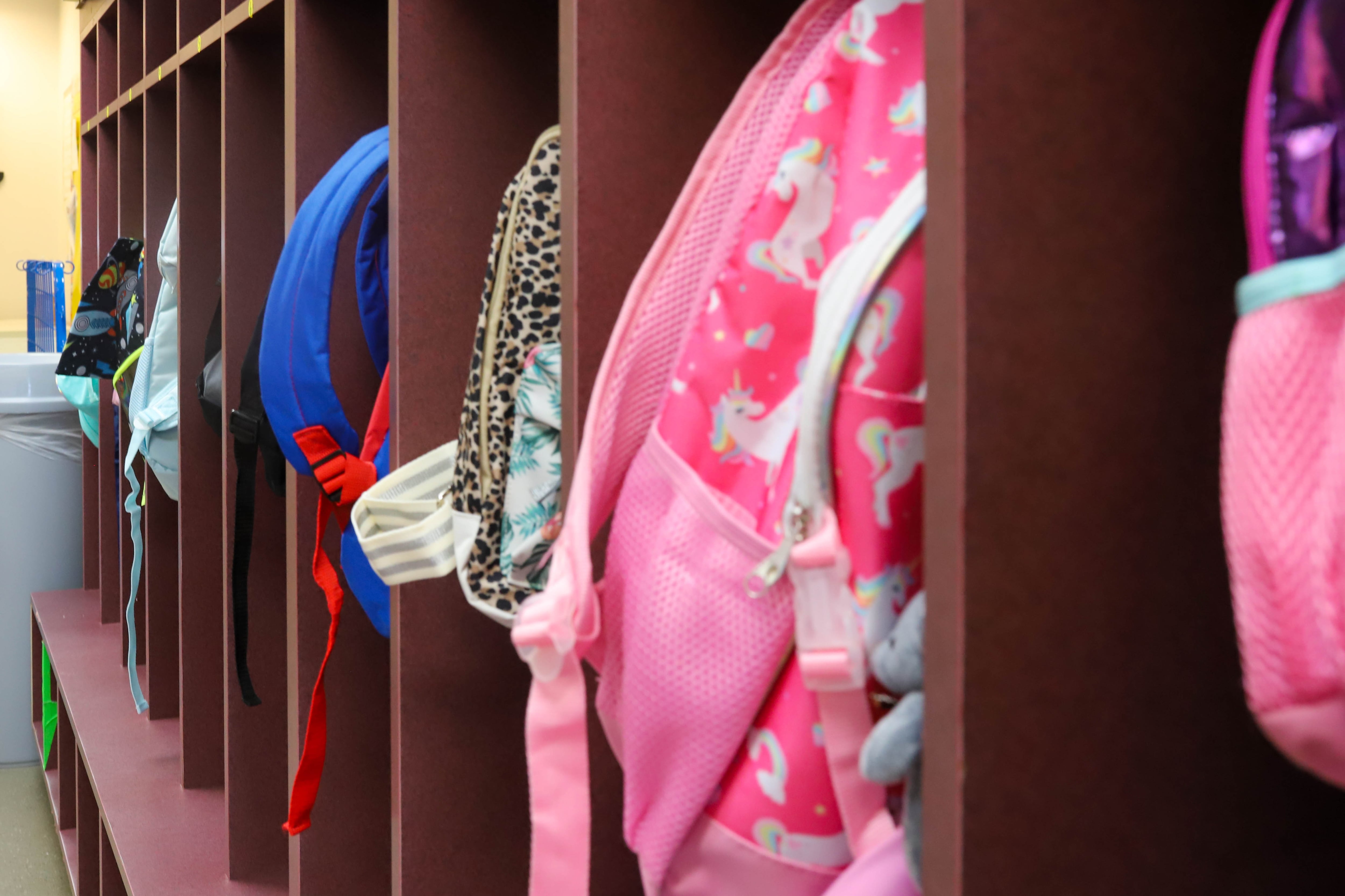 A child’s pink backpack hangs off a coat rack.