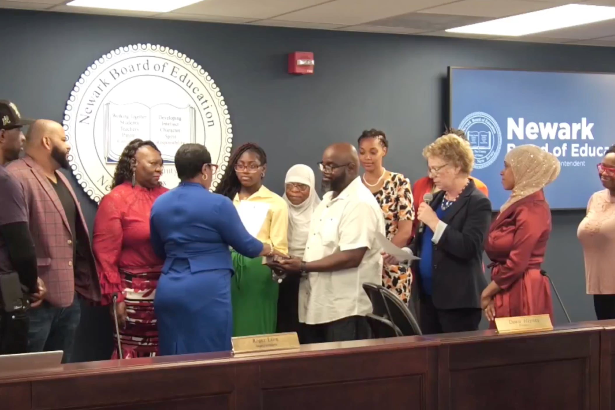 People stand behind a large desk as a school board member is sworn into office.
