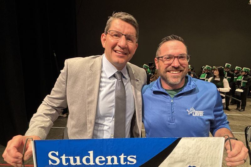 Two men with glasses hold a banner.