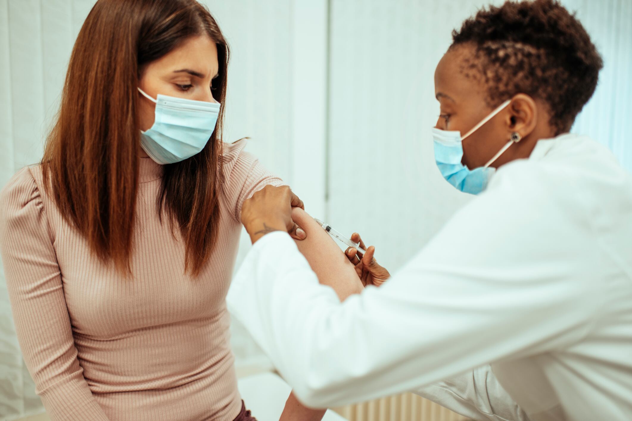 A doctor administers a vaccine to a patient. Both are wearing blue face masks.