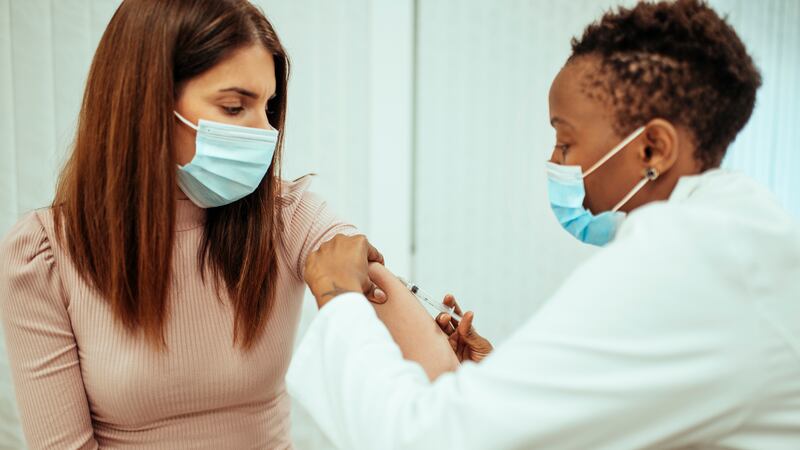 A doctor administers a vaccine to a patient. Both are wearing blue face masks.