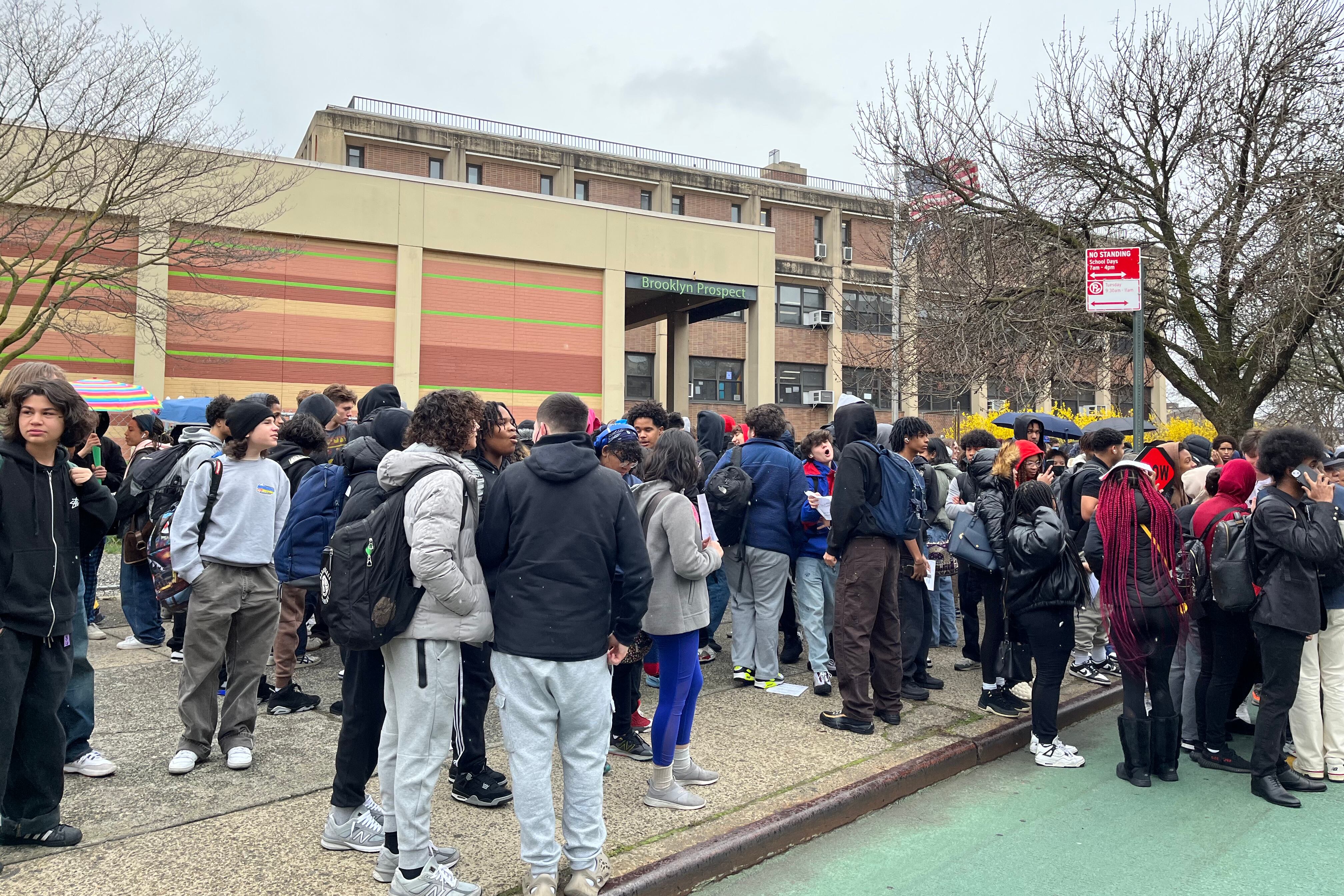 Hundreds of high school students stand outside of a school building.