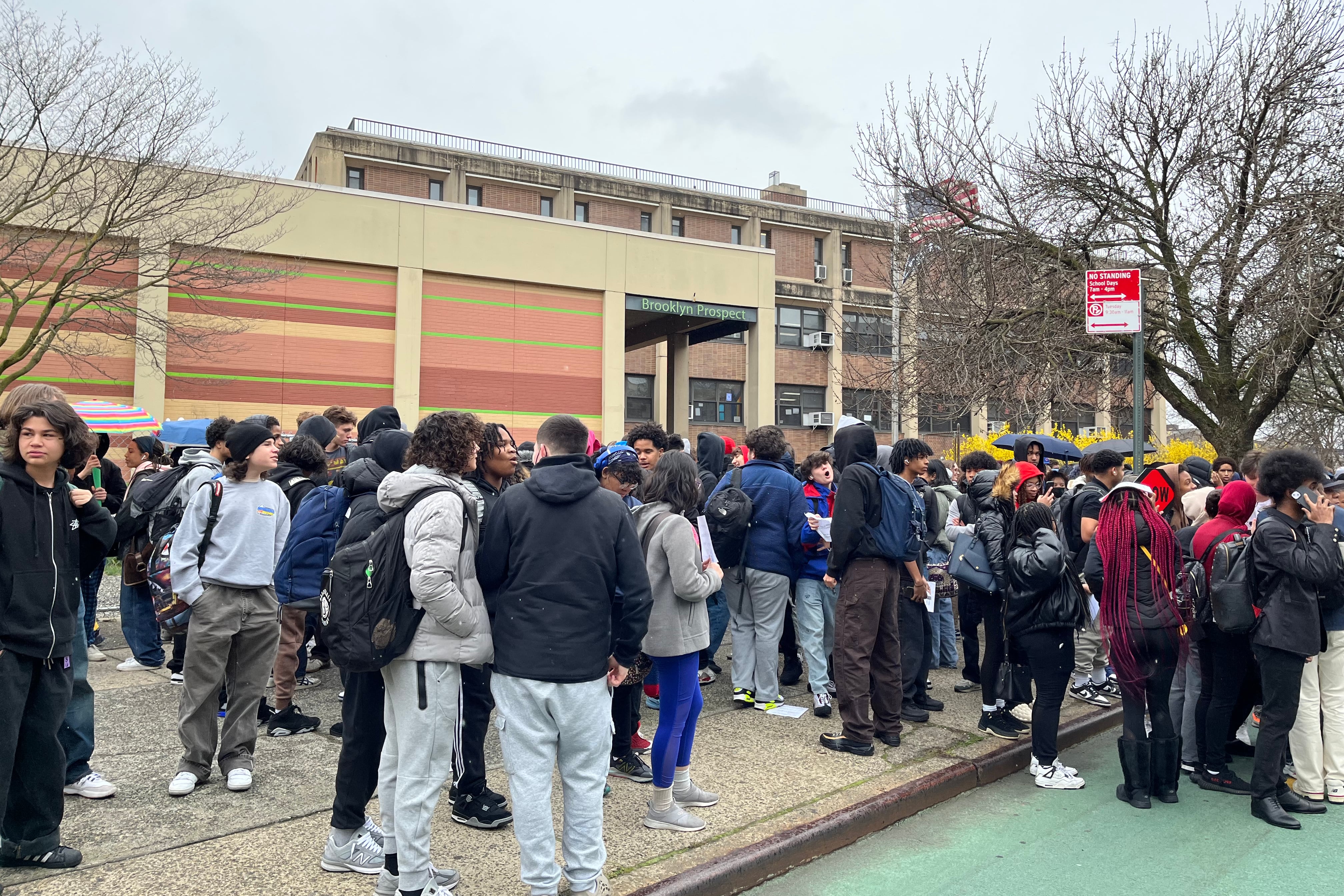 Hundreds of high school students stand outside of a school building.
