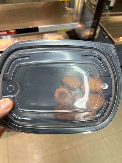 A black plastic container with a see-through lid has seven veggie nuggets.