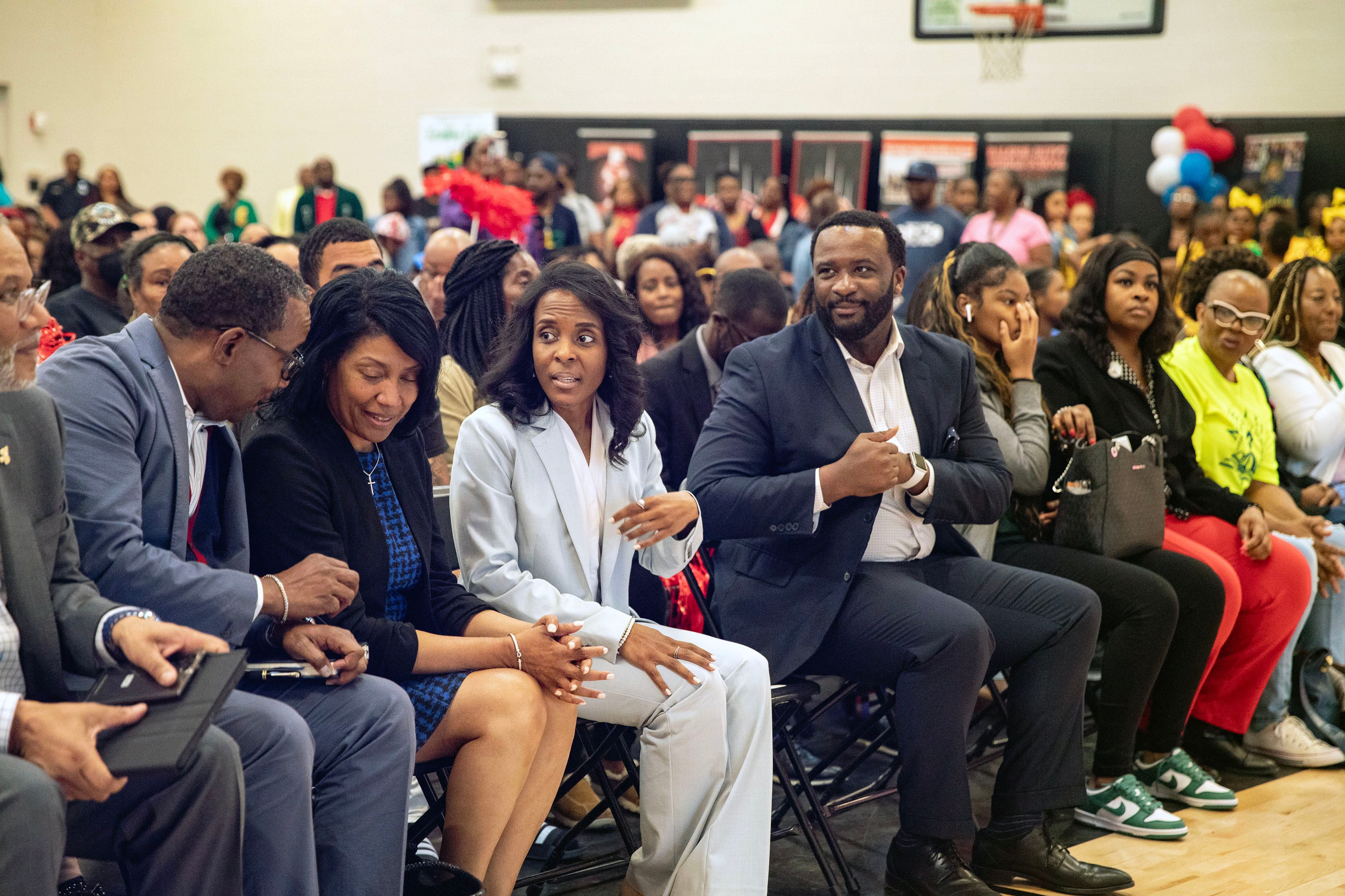Rows of people sit in chairs in a school gym.