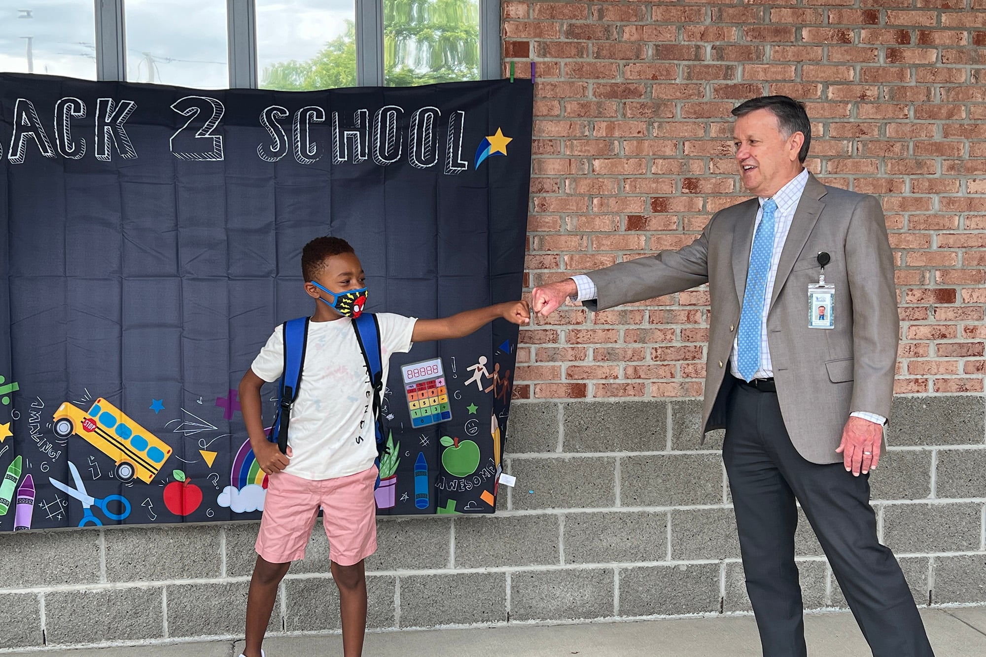 A man fist bumps a student in front of a school.