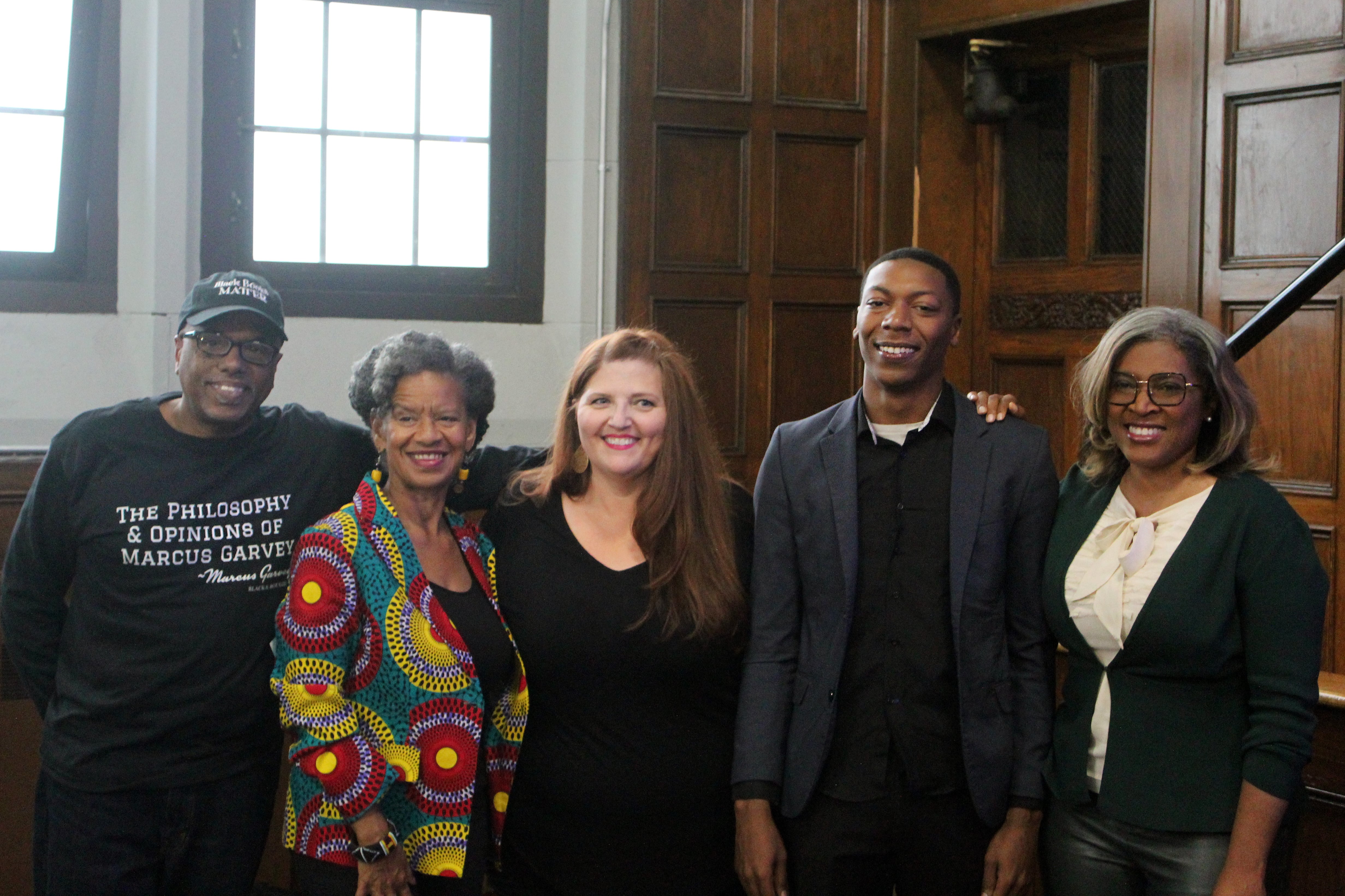 A tall young man wearing a sportcoat and standing in a room near some windows, flanked by four other adults, all facing the camera.