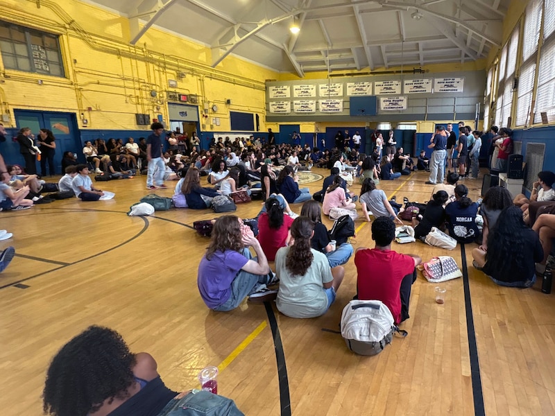 A large group of high school students sit in a school gym.