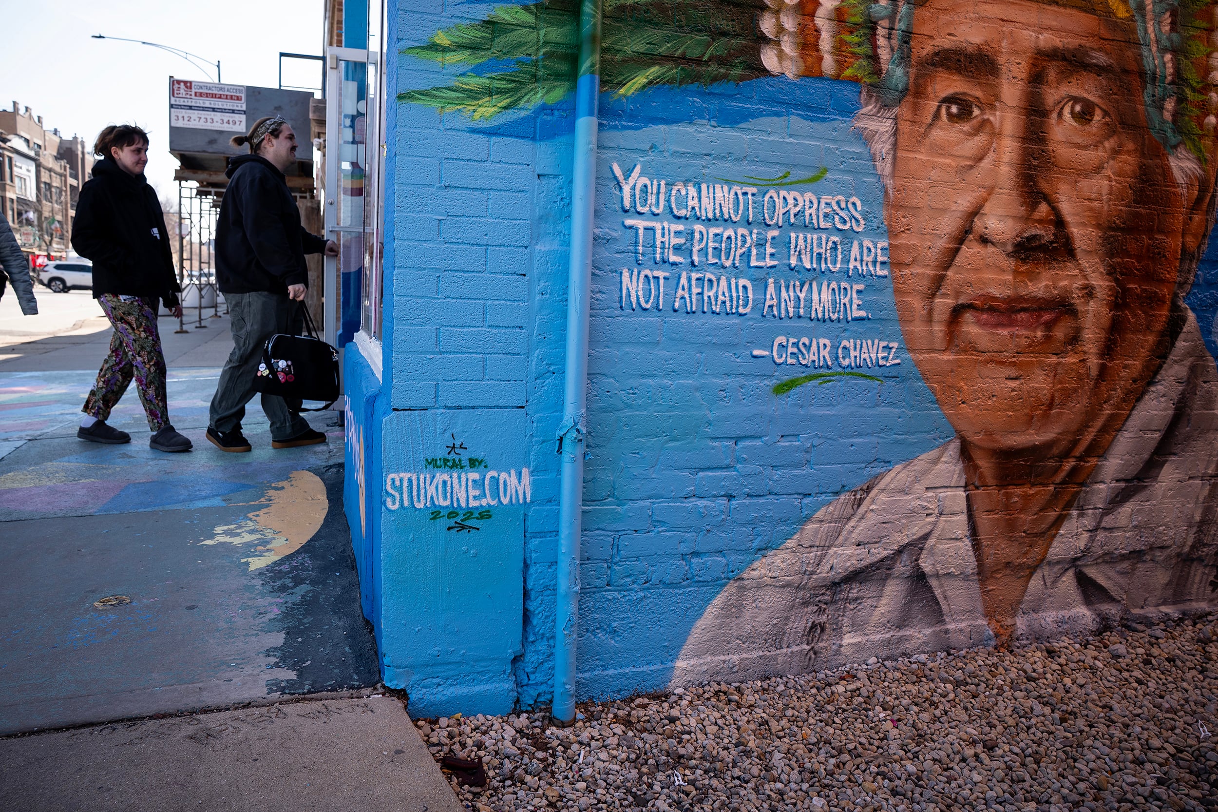 A photograph of a mural on a blue brick wall with a couple of people in the background.