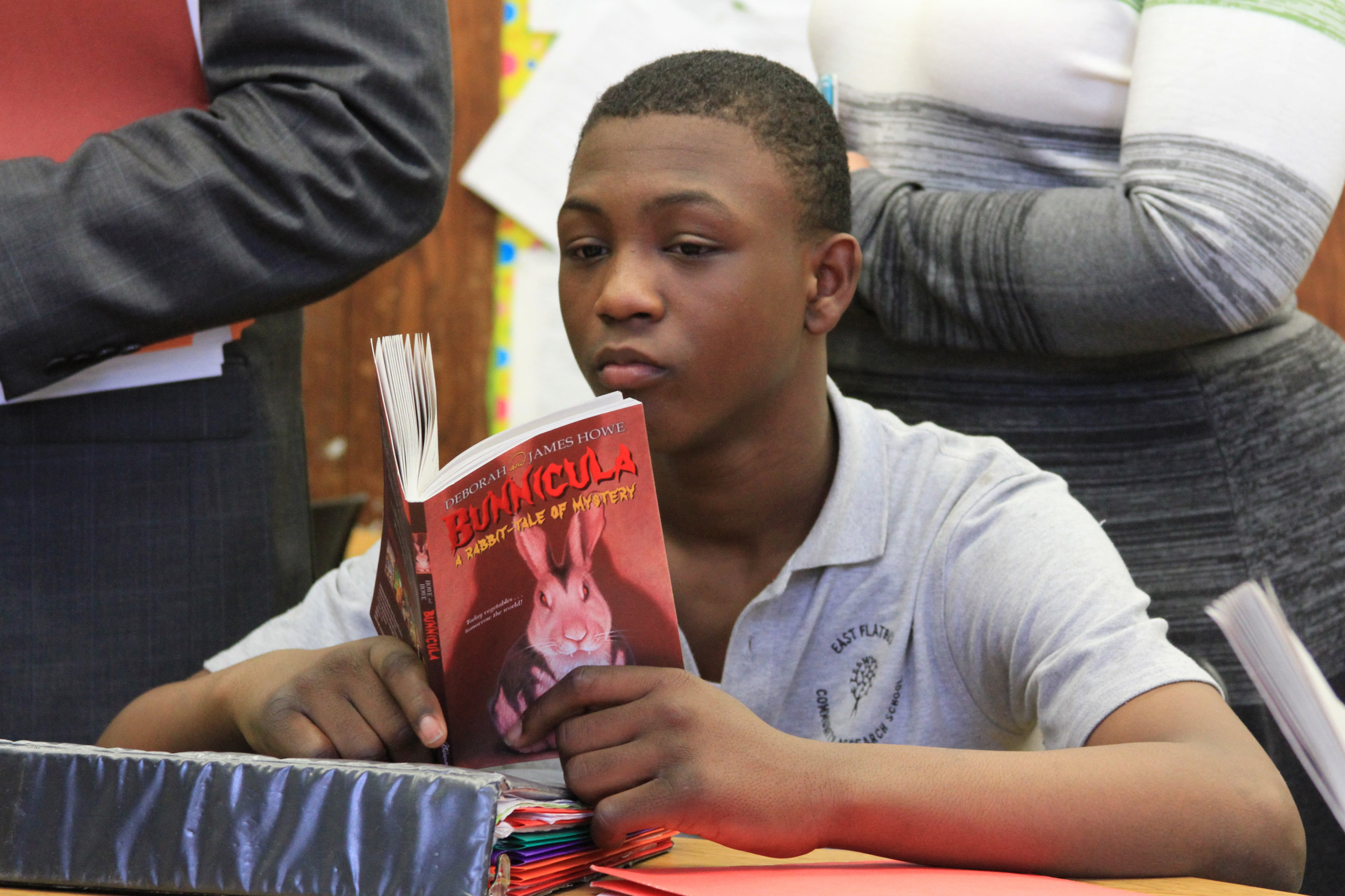 A boy in a blue school uniform sits at a table reading a book.