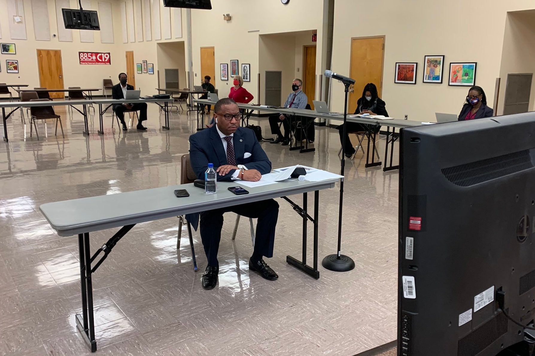 Superintendent Joris Ray sits at a table in the central office auditorium looking at a screen to join the virtual school board committee meeting.