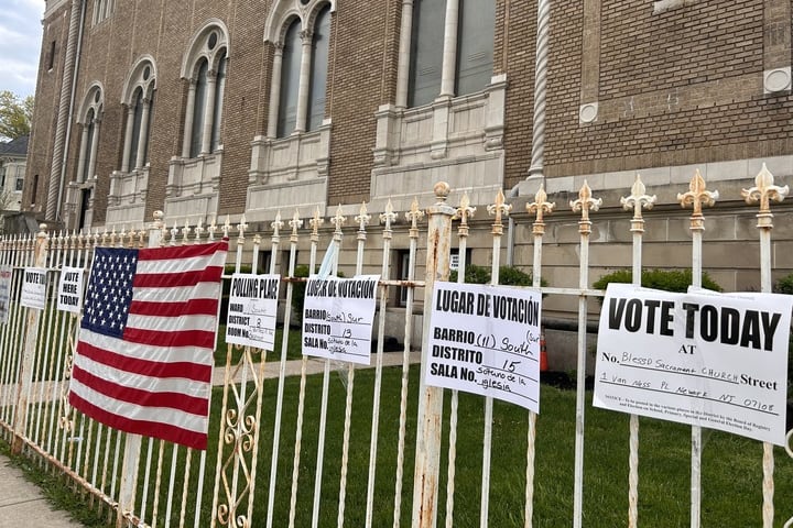 Signs reading “vote today” hangs from a white fence next to a united states flags.