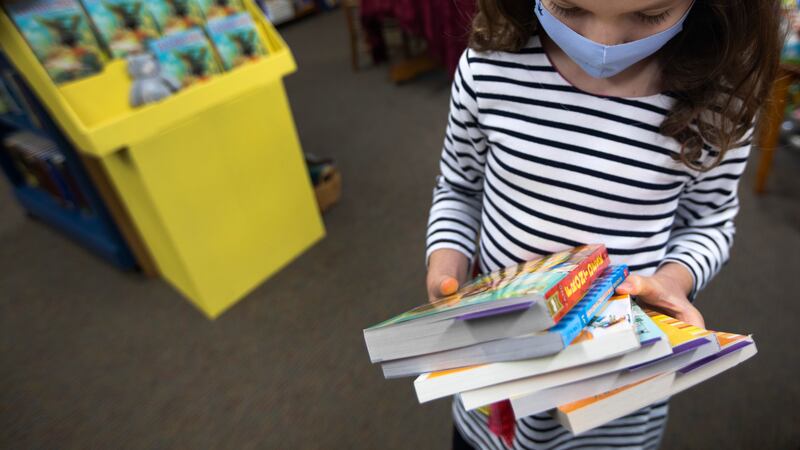 A masked child looks at her armful of books she holds inside the Once Upon a Time bookstore in Montrose.