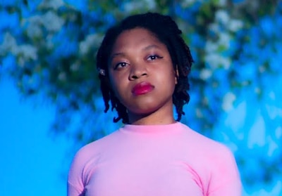 Headshot of a woman wearing a pink shirt. There is a tree in the background.