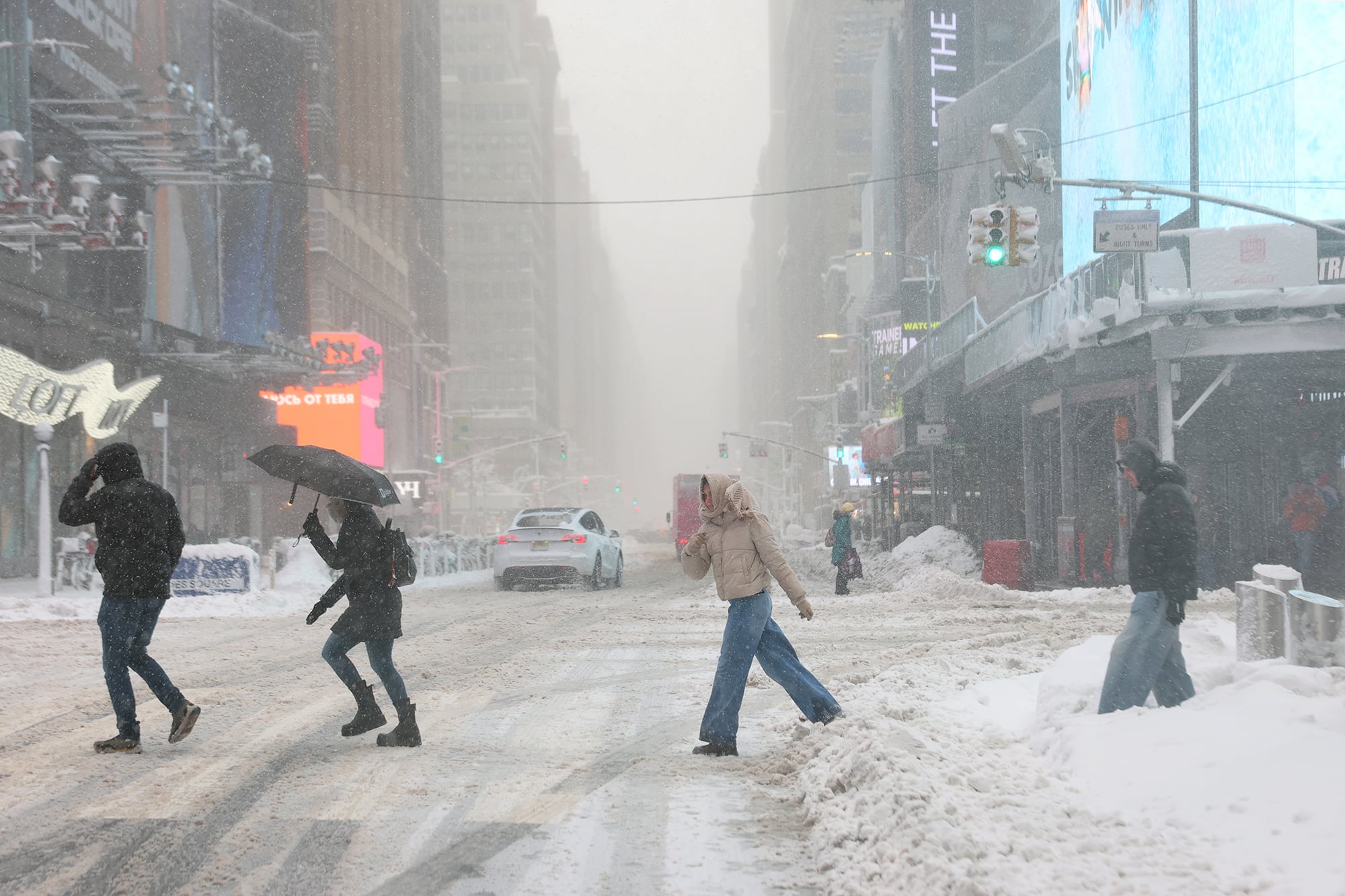 Four people cross a snow covered street with low visibility of buildings in the background.