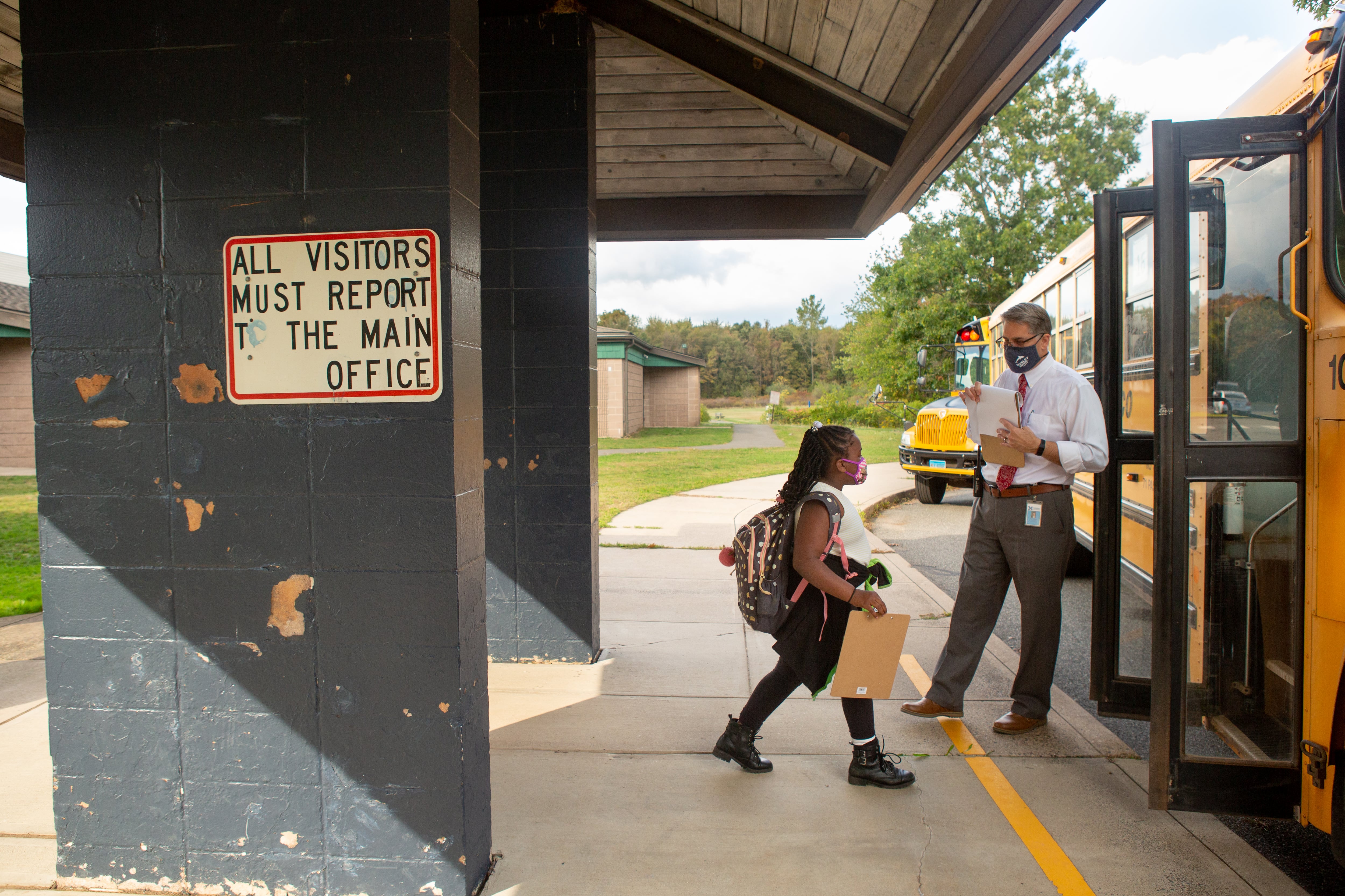 A student walks toward the open doors of a school bus while an employee stands near the door.