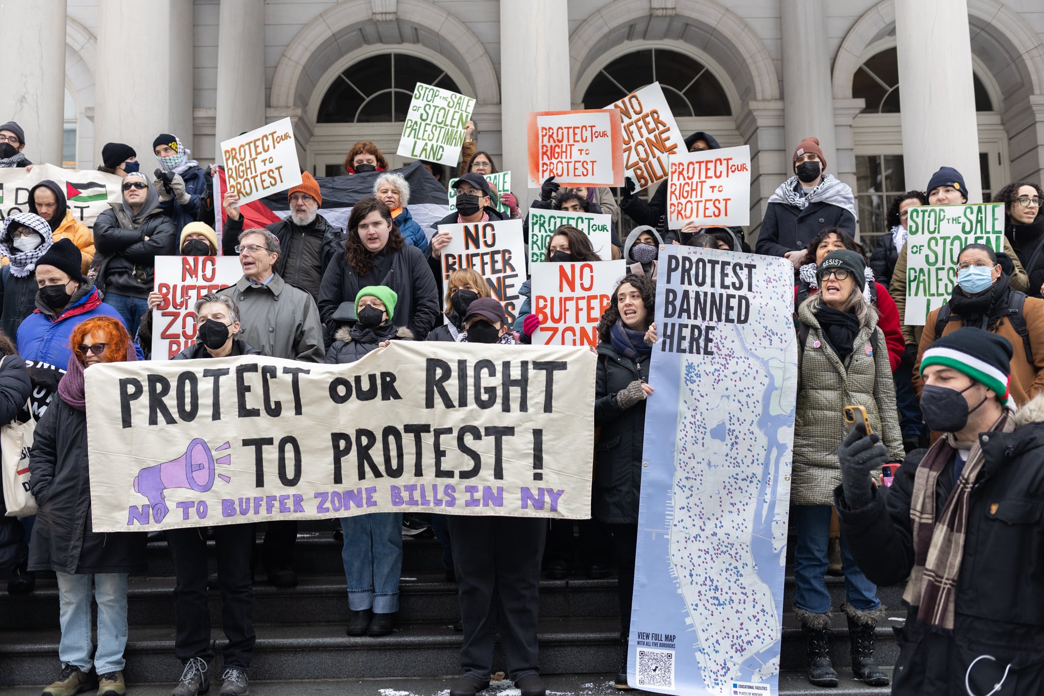 A group of people holding protest signs stand on the steps of a building.