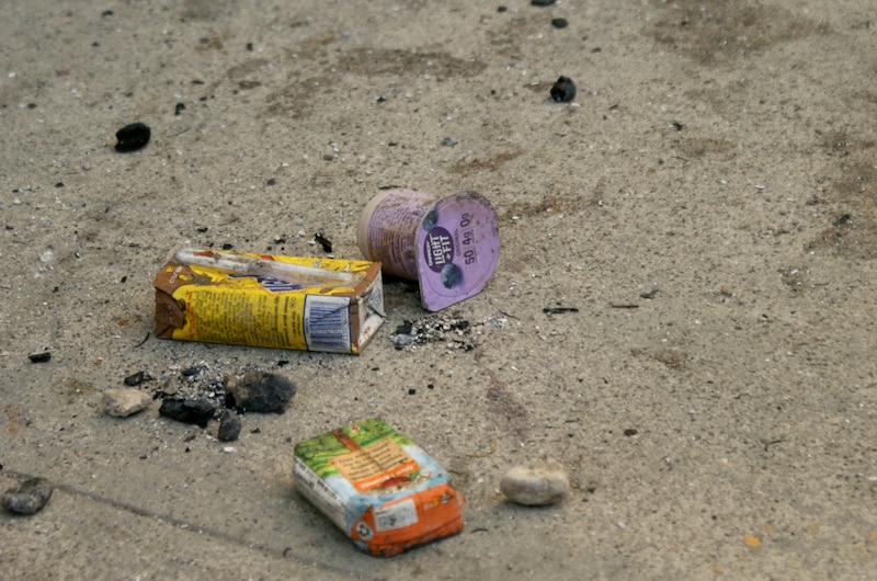A milk, juice and yogurt container covered in ash and dirt on concrete outside.