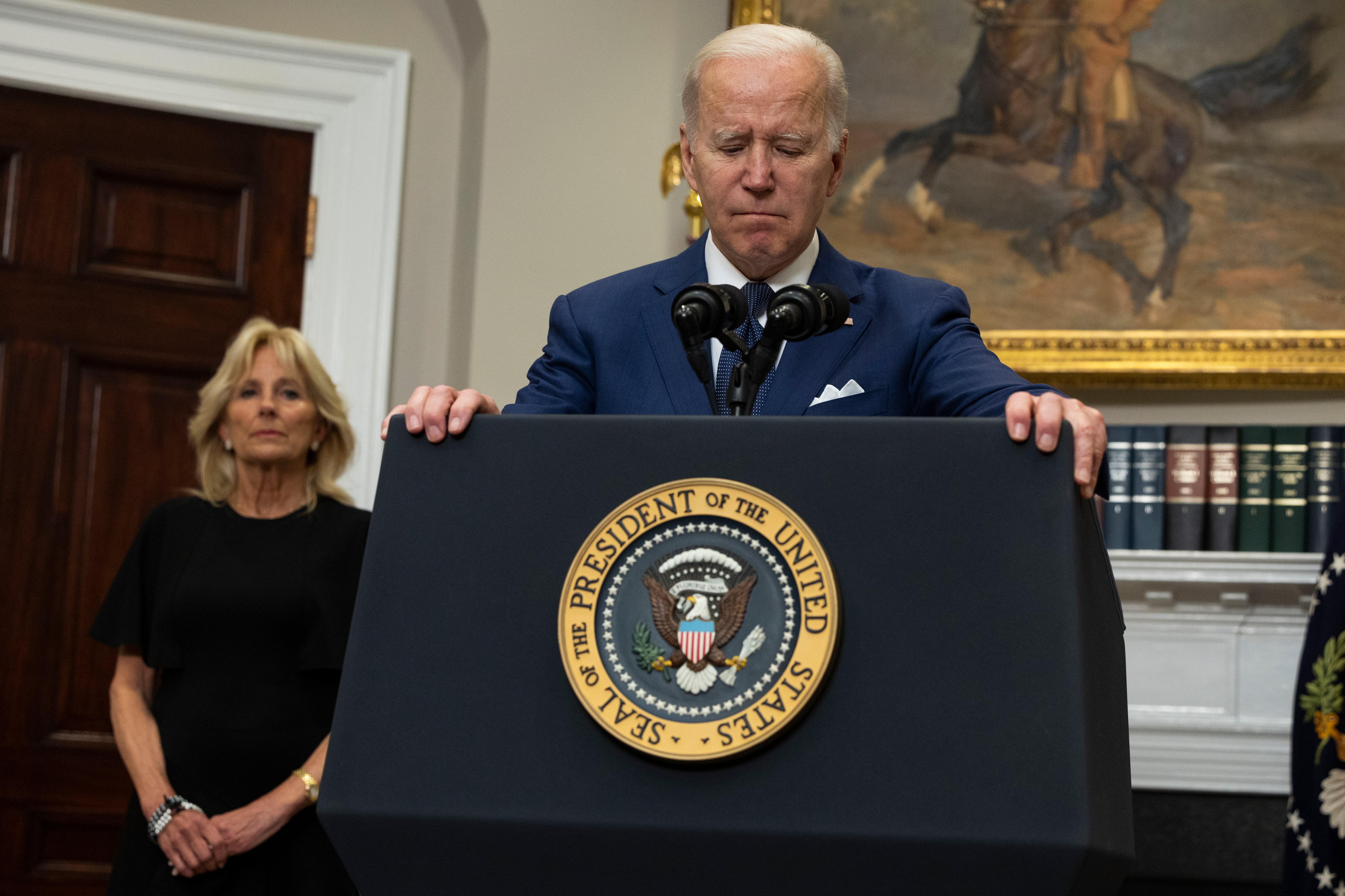 President Joe Biden clutches a podium during a speech to the nation, his wife Dr. Jill Biden stands behind his right shoulder.