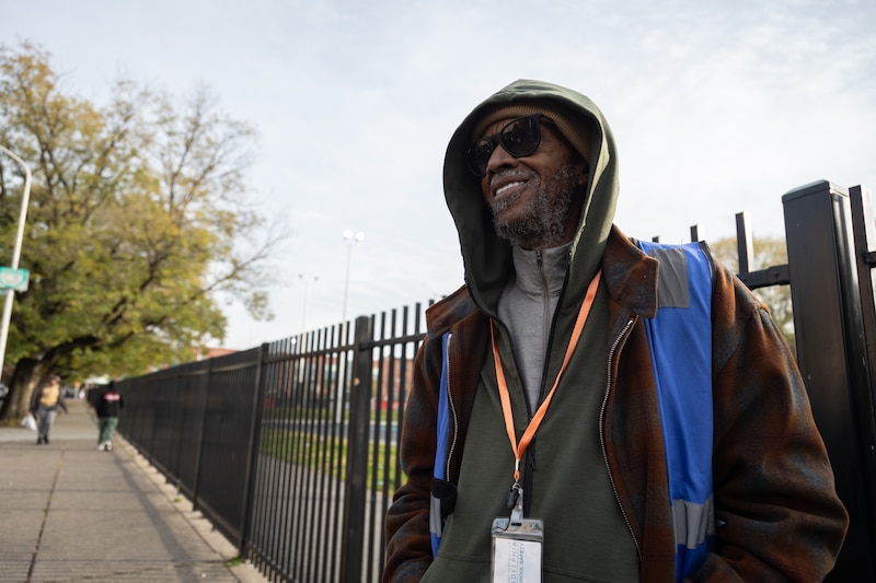 A man in a hoodie stands in front of a fence.