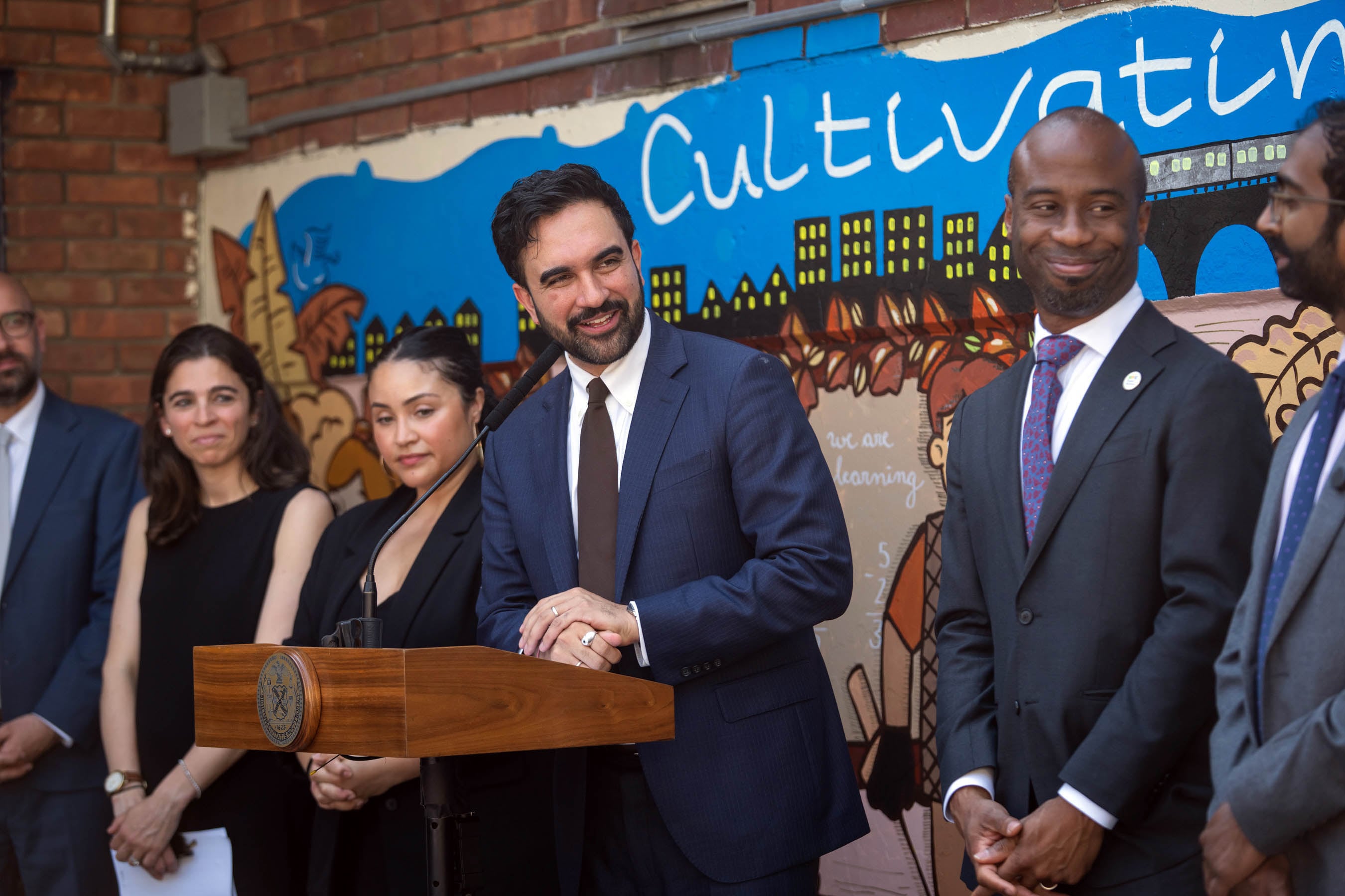 A photograph of a group of adults in suits standing behind a podium in a school.