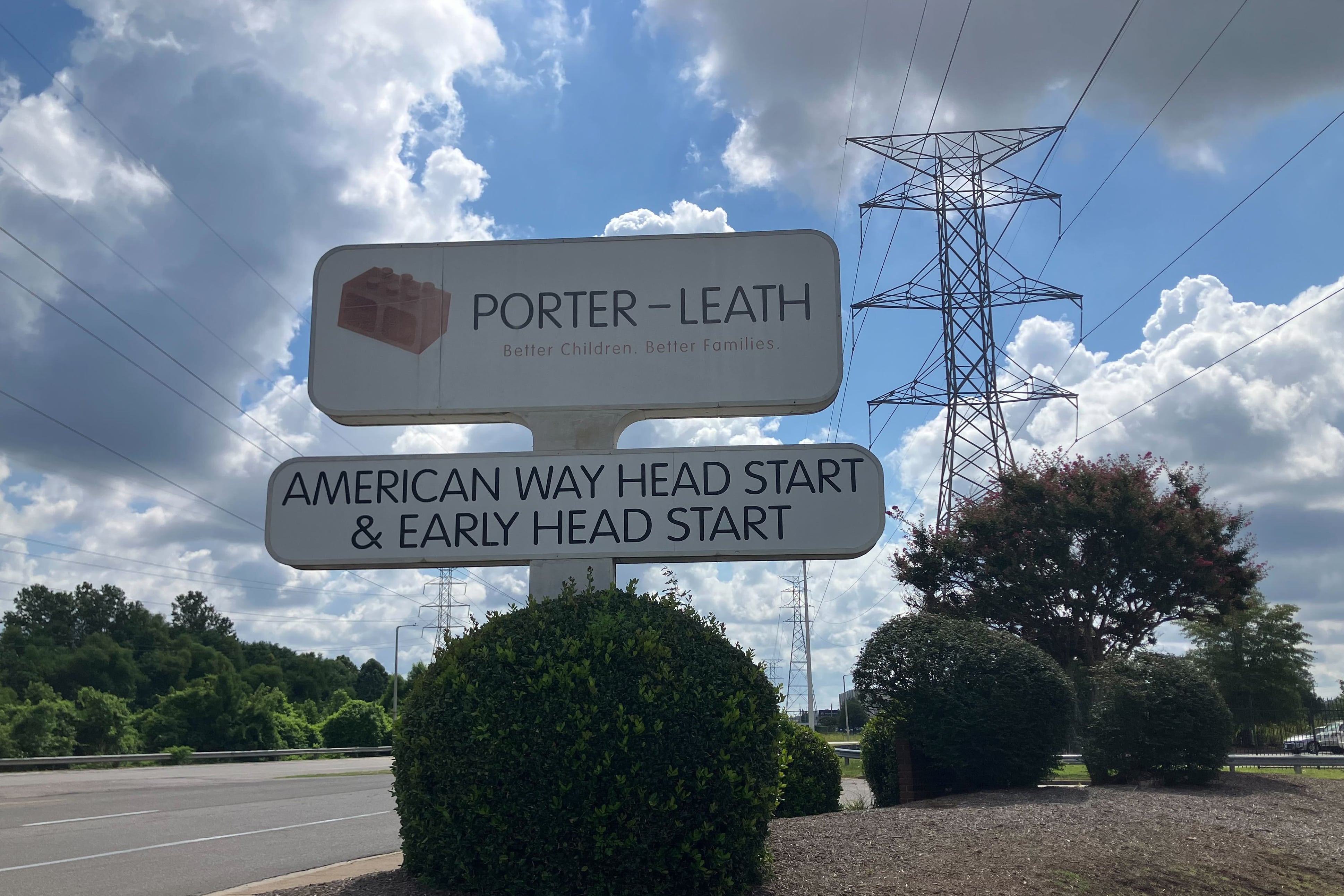 A photograph of A sign outside on a sunny day with large white clouds in the sky.