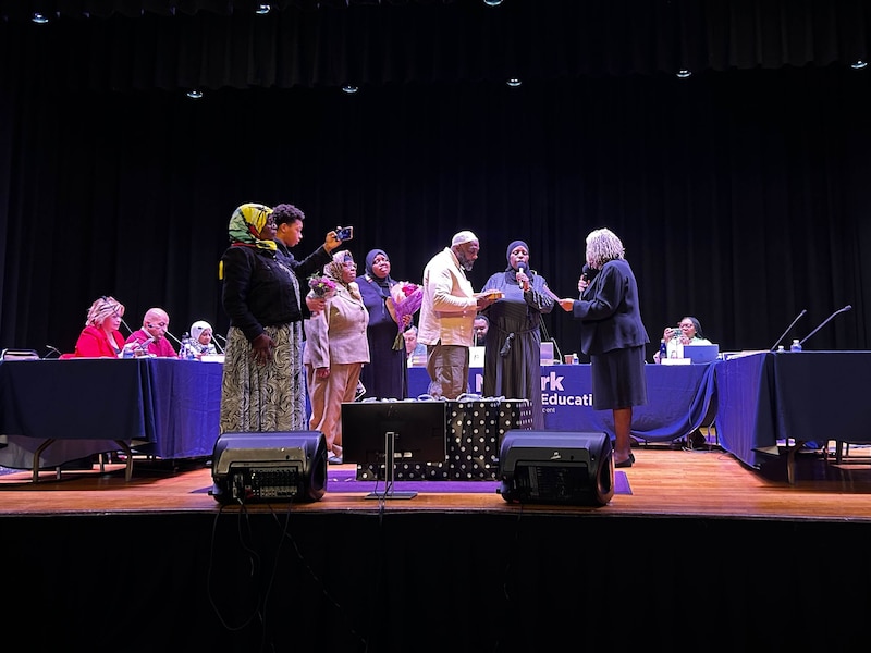 People stand on a stage with tables in the background.