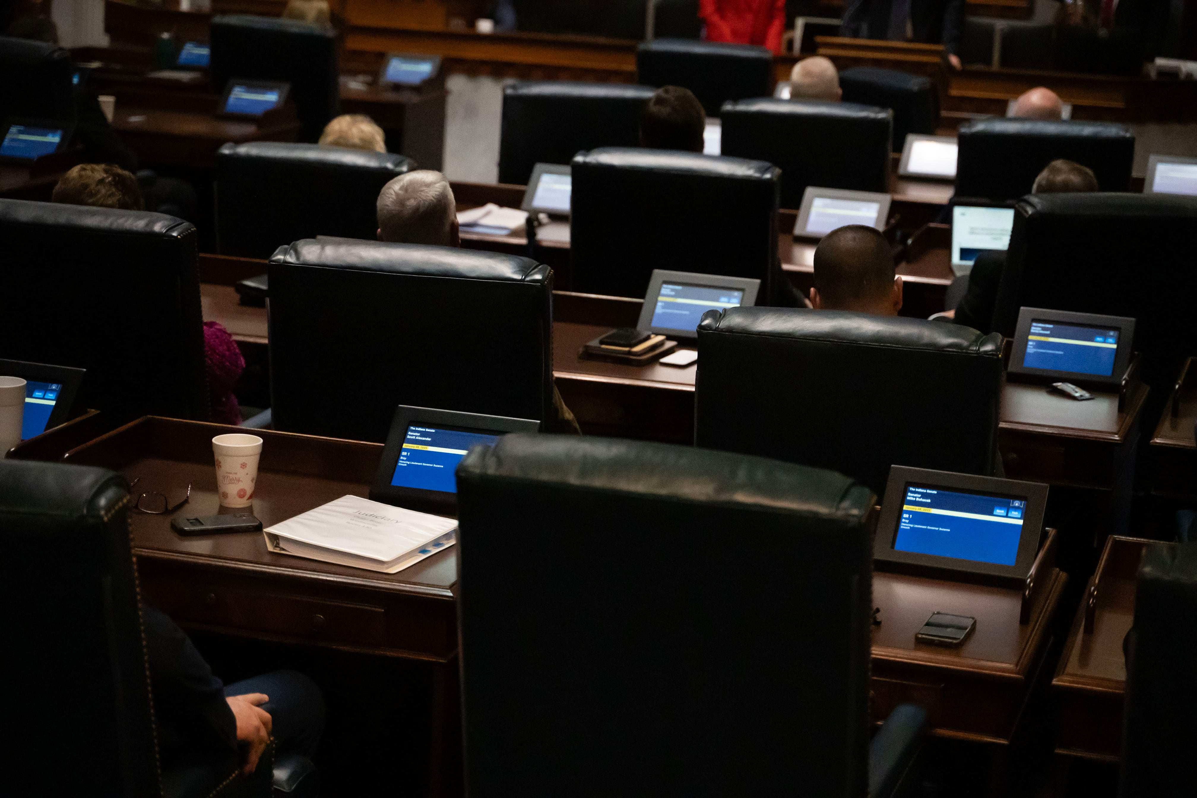 A room full of people in business clothes sit at chairs in rows of wooden desks in a large room.