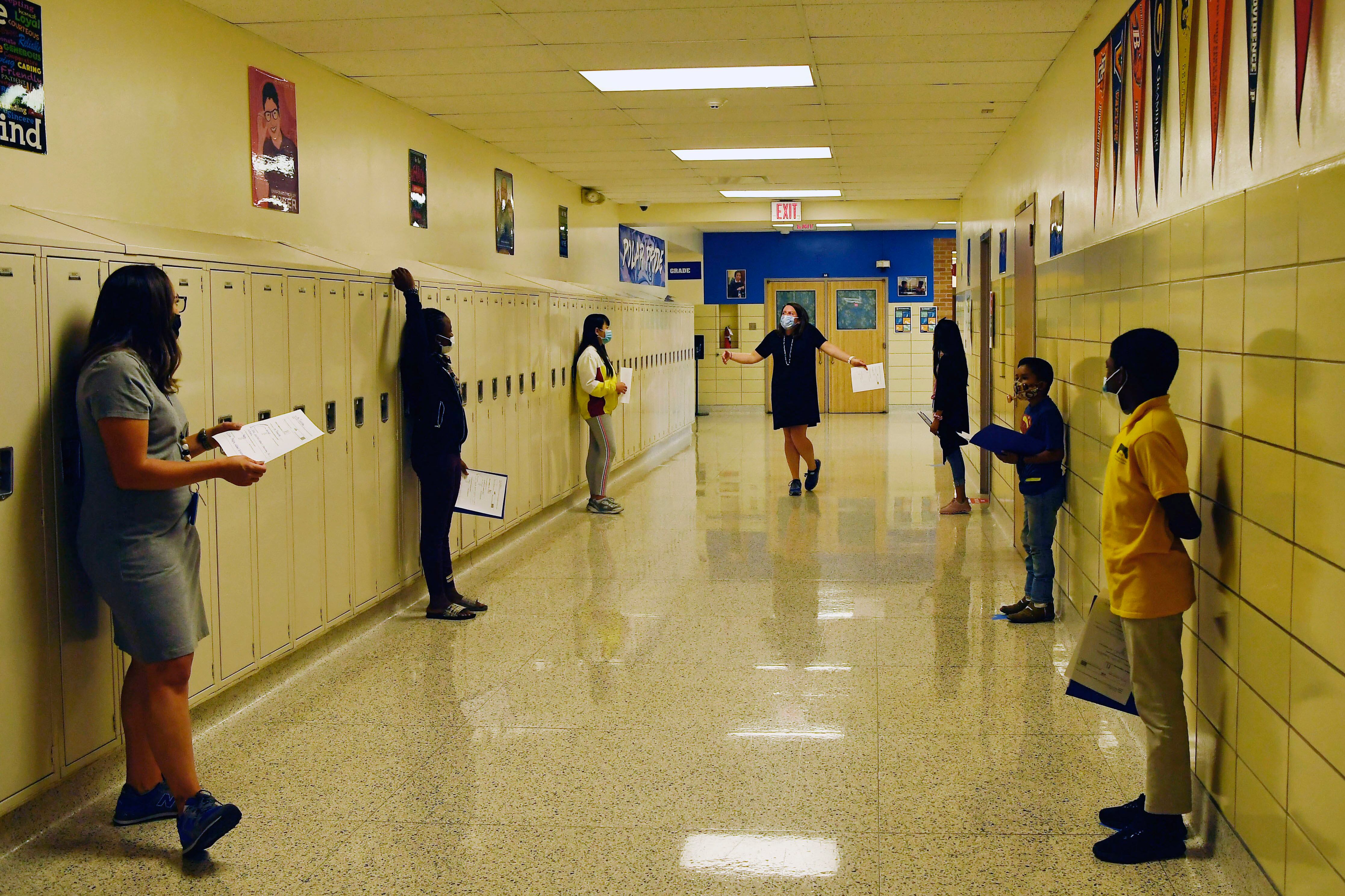 Middle school students are spaced out in a hallway with lockers, during a conversation exercise.