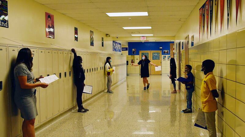 Middle school students are spaced out in a hallway with lockers, during a conversation exercise.