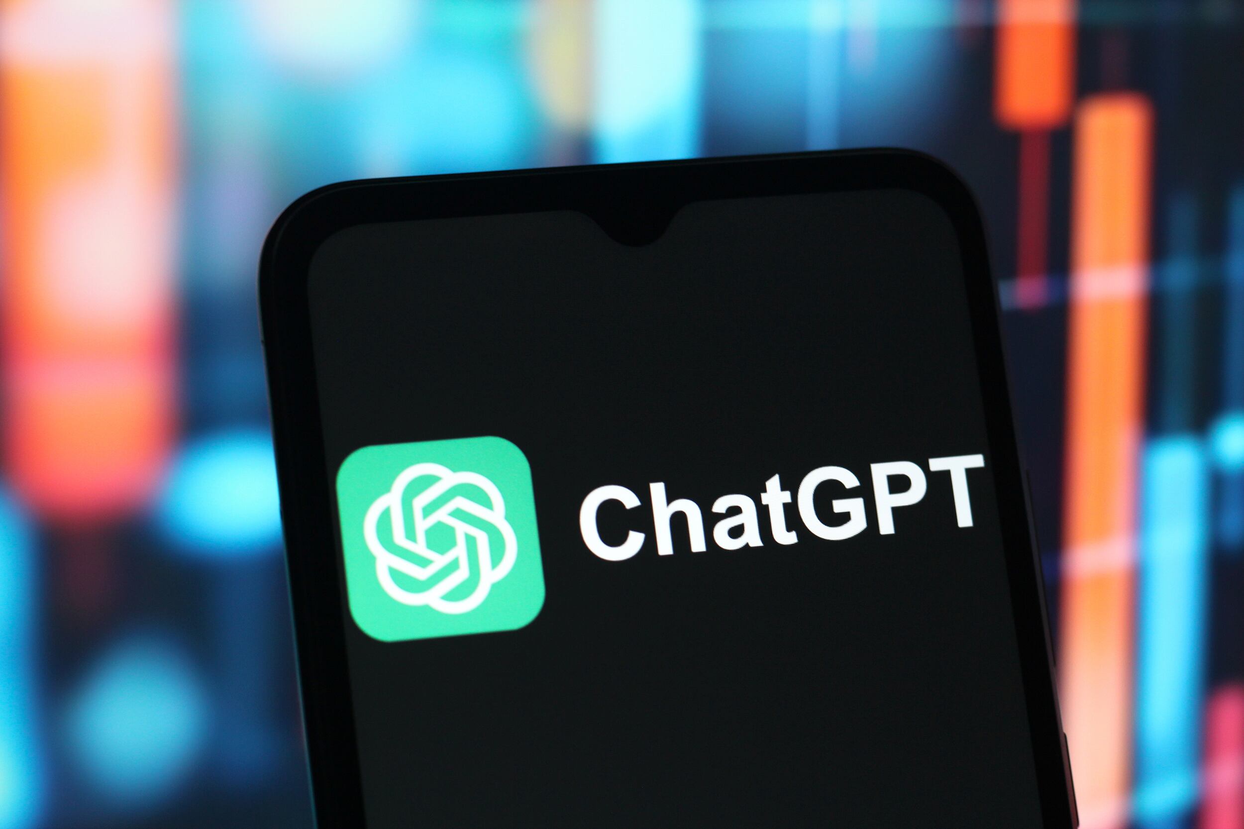 In this photo illustration, there's a cellphone with the words "ChatGPT" on it against a colorful background.
