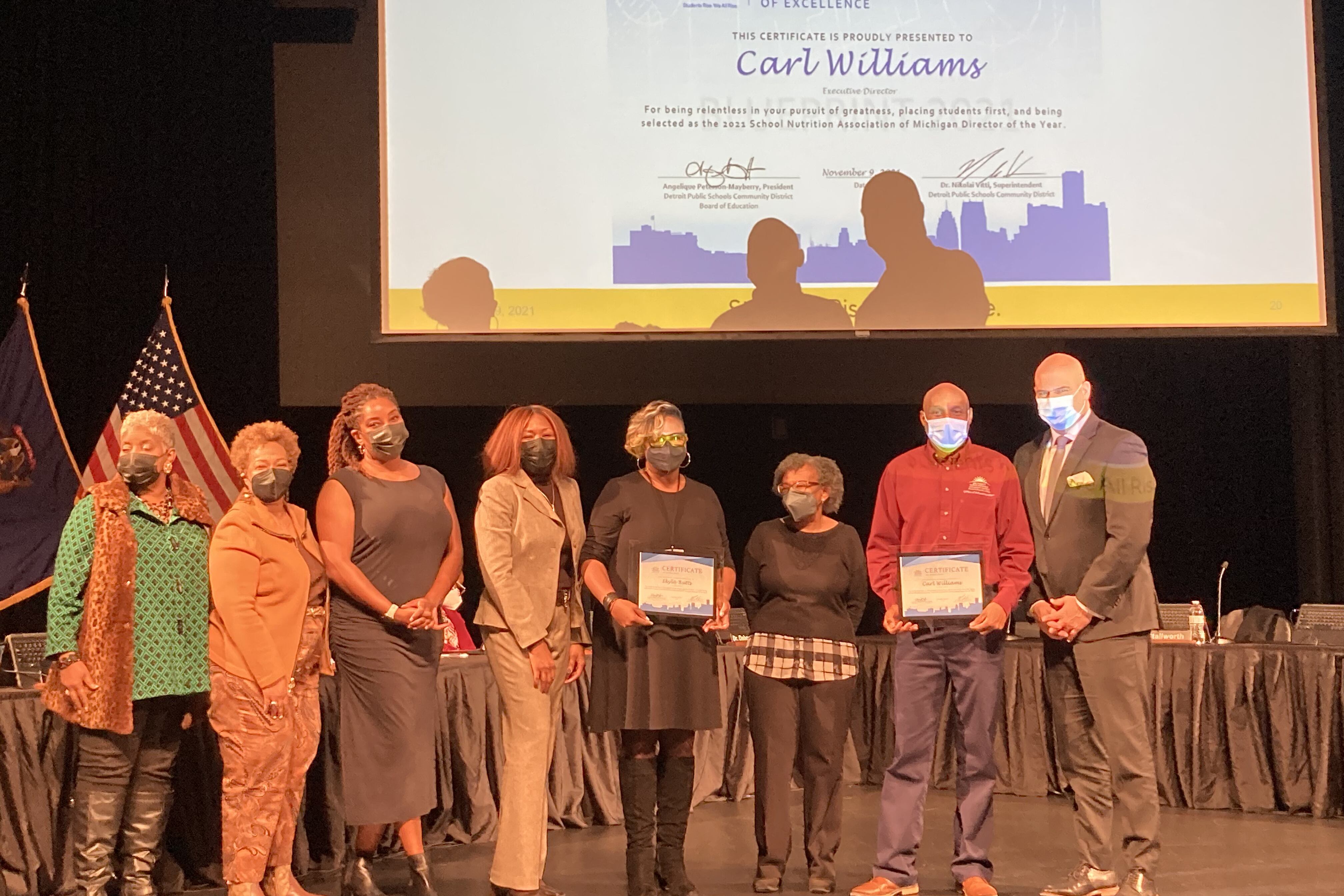 School board members and administrators in the Detroit school district take a photo during a school board meeting with two employees who won top honors in a statewide recognition program.